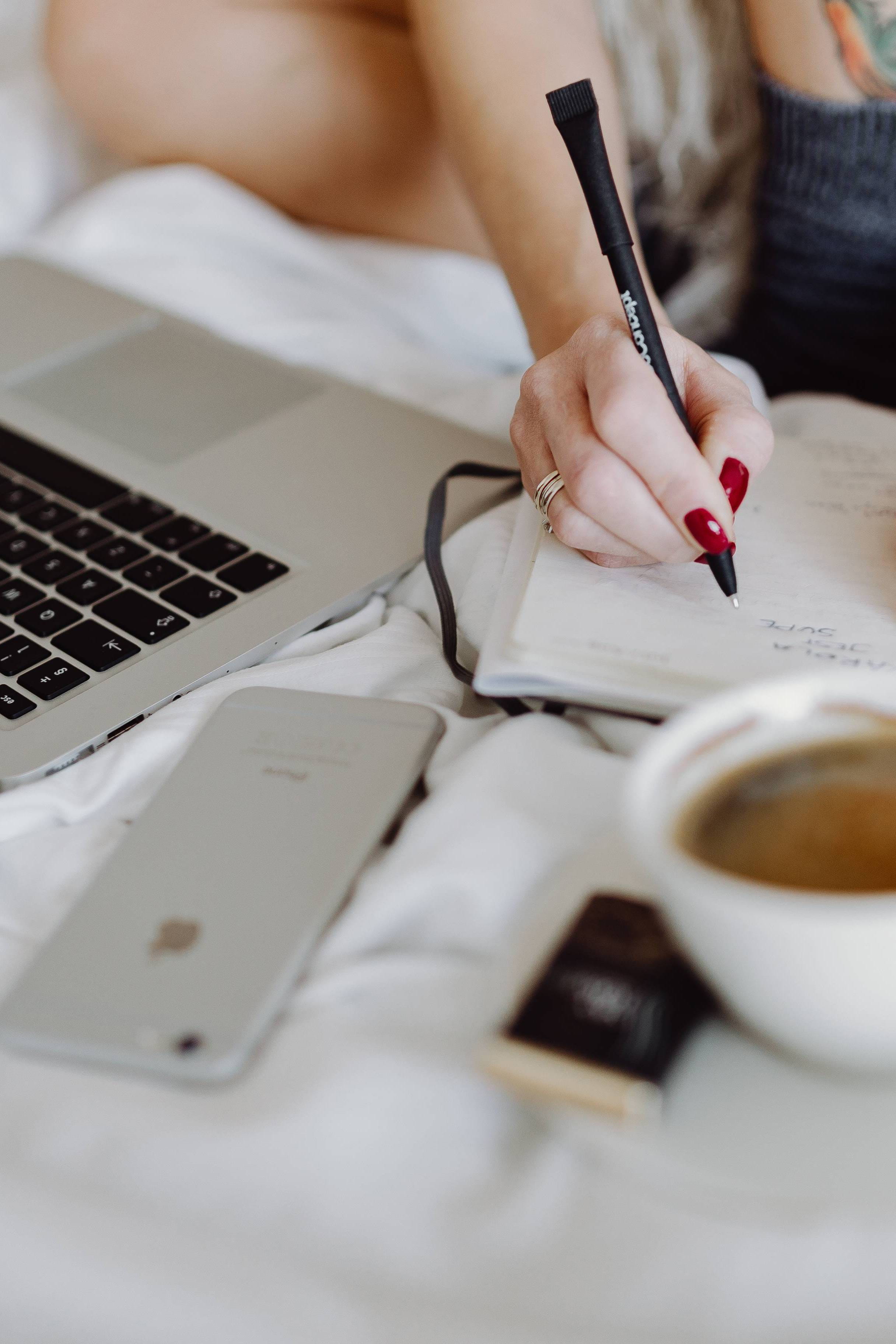 Woman working on a laptop while enjoying a breakfast coffee and chocolate in bed