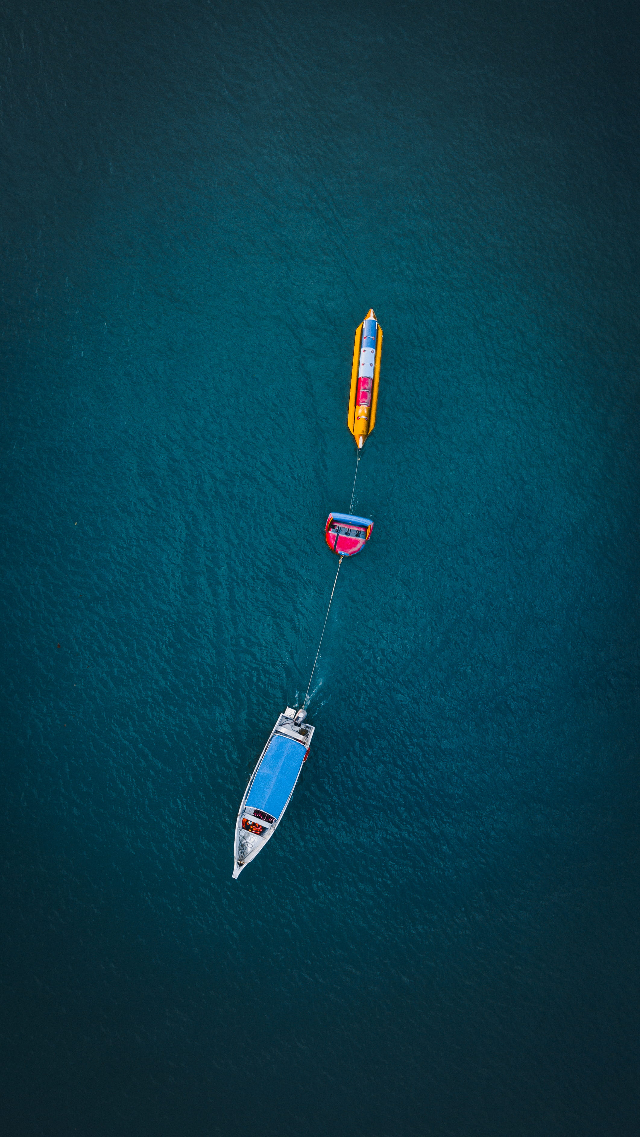 white and yellow boats on body of water, aerial view of boat pulling banana boat