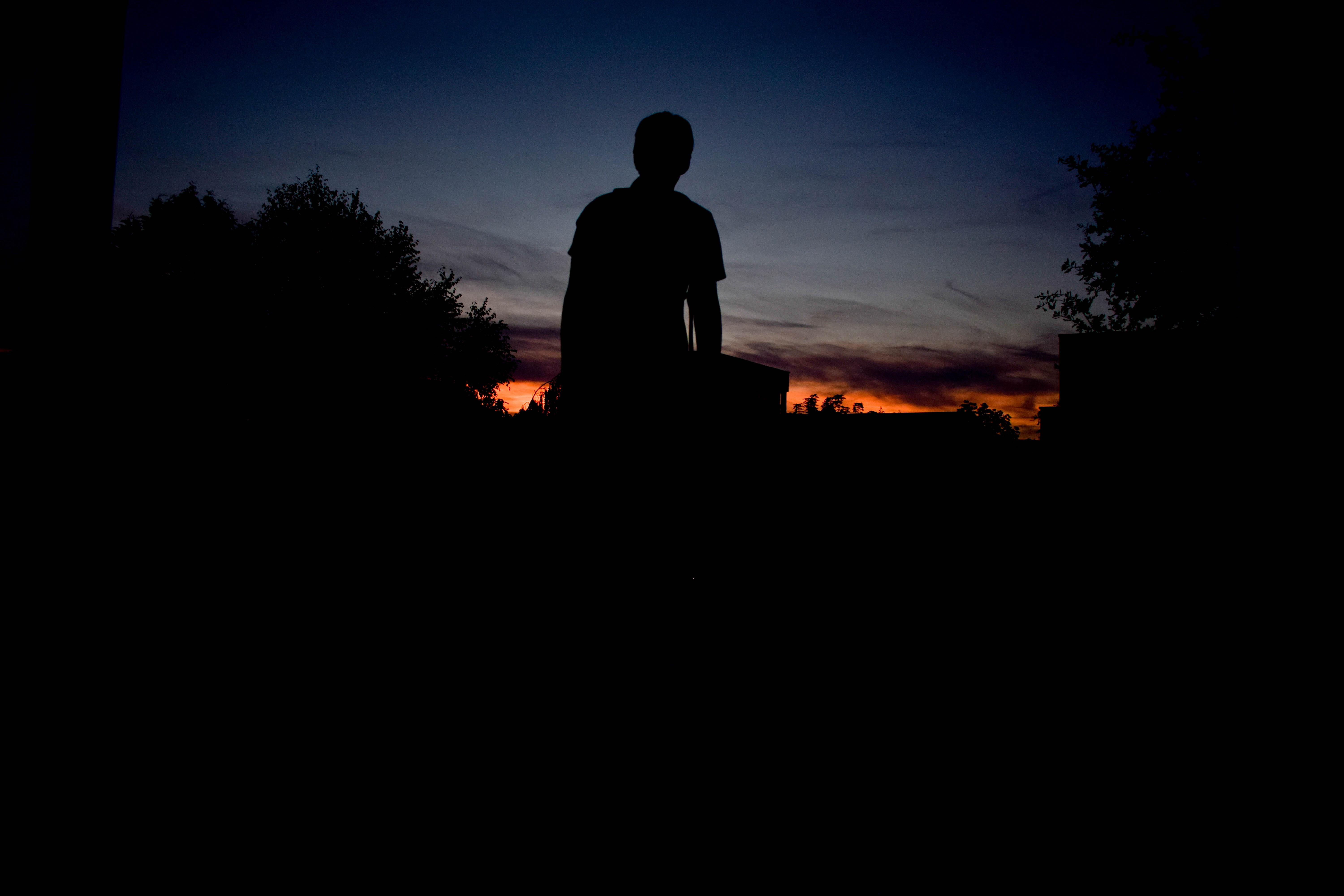 silhouette of person standing under blue sky during sunet, person standing between tress silhouette