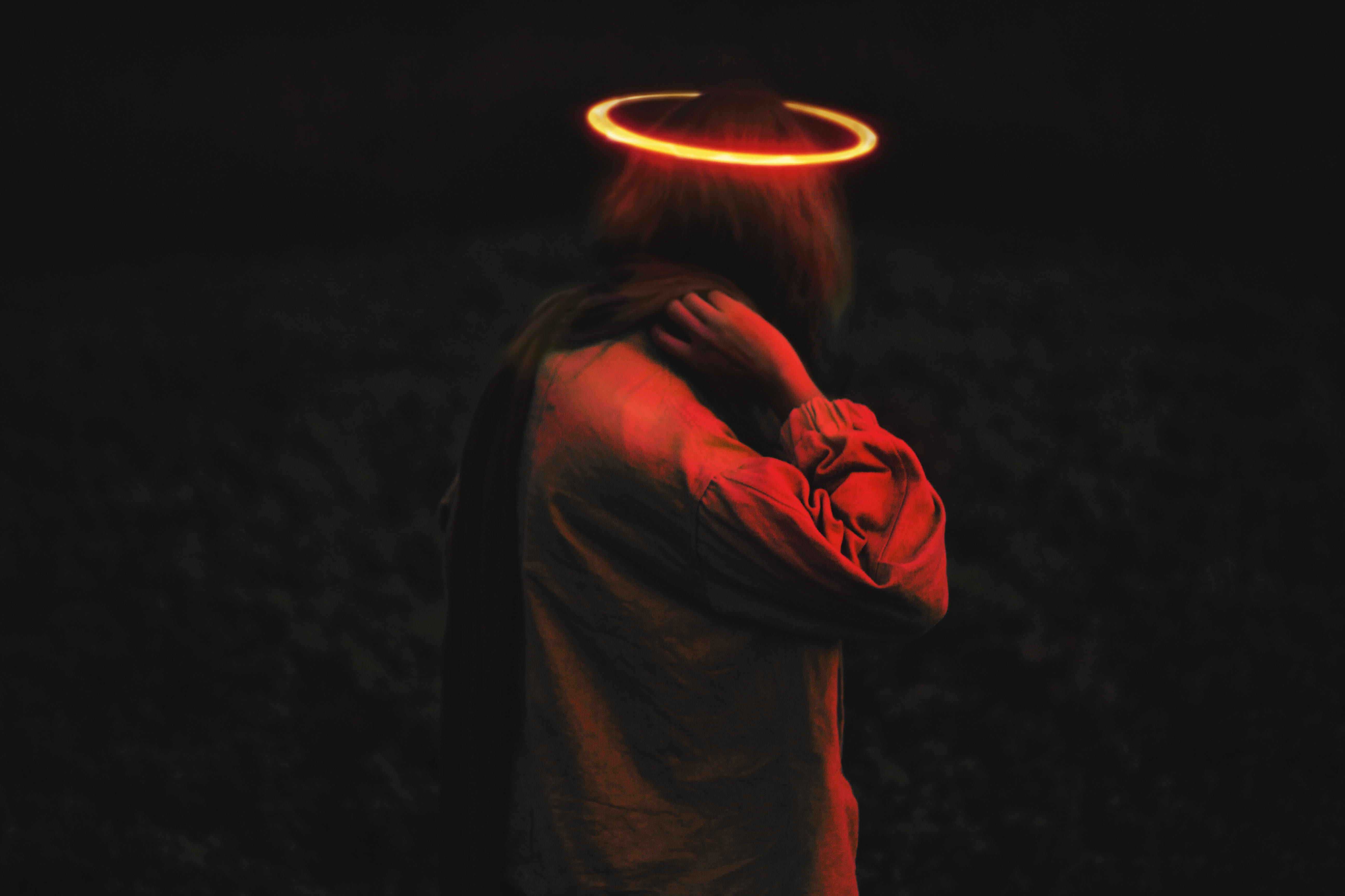 person wearing long-sleeved top with halo, person with hands on nape in dark lit room