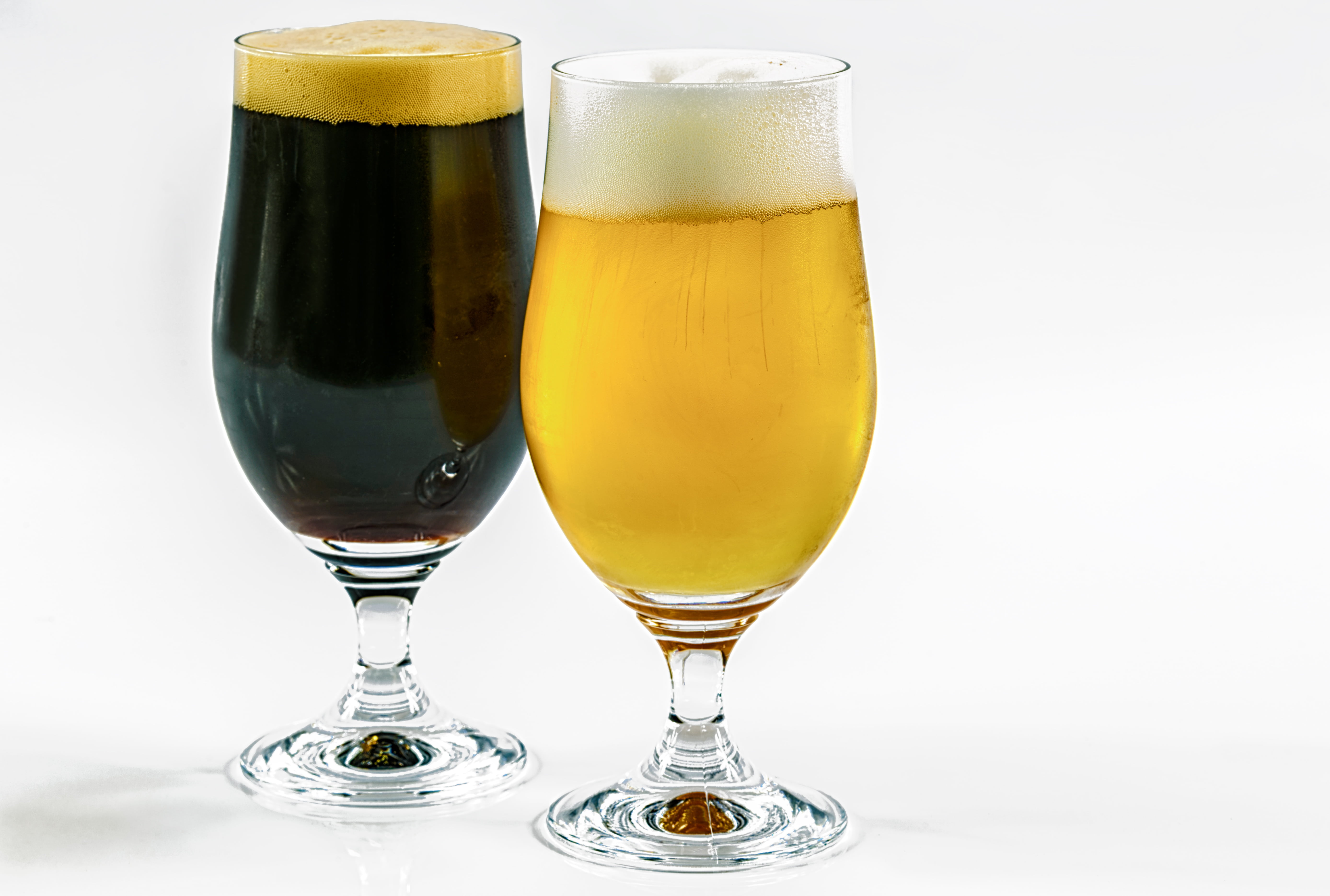 two clear footed drinking glasses, two types of beer, dark, caramel