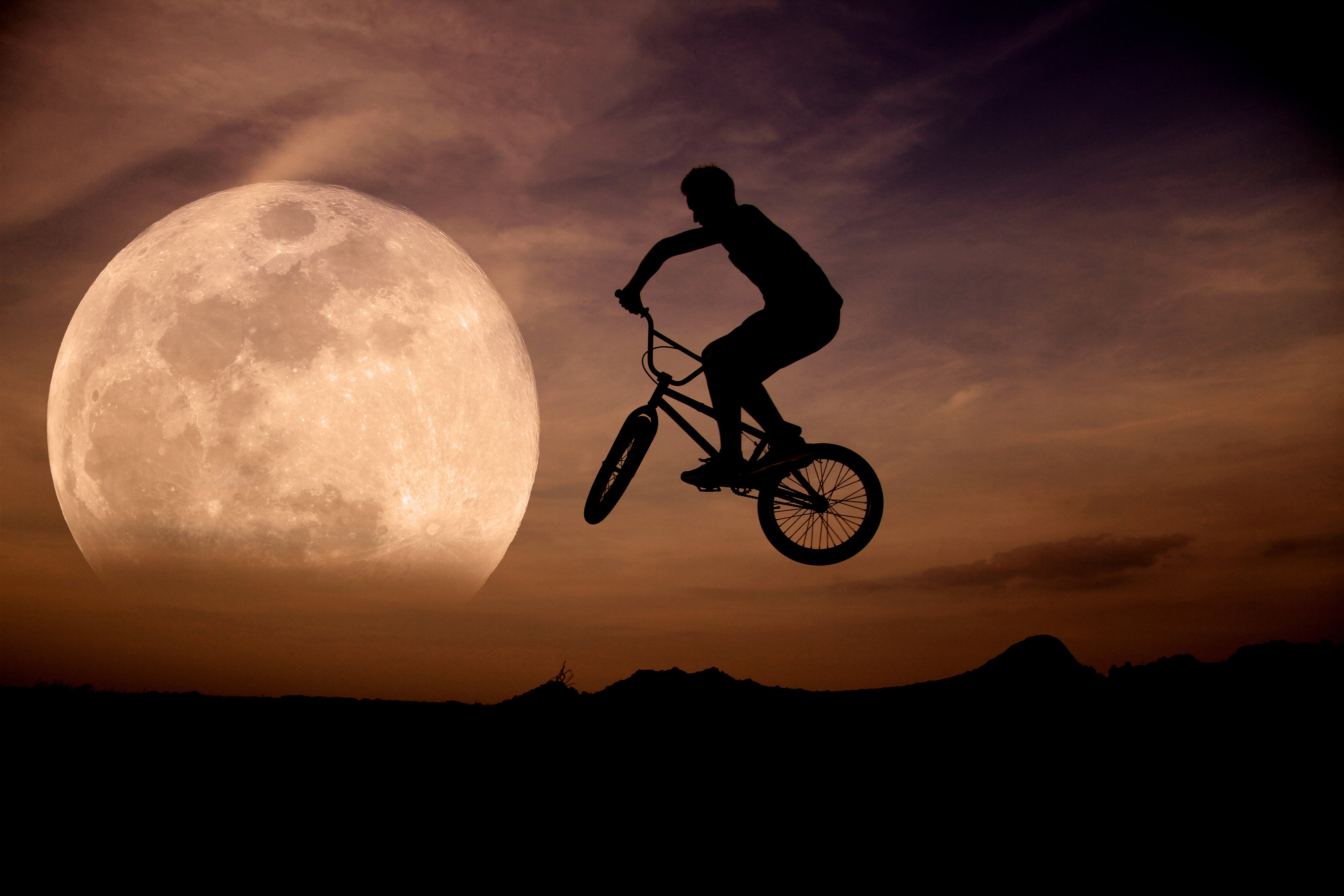 silhouette of man riding bicycle on mid air during sunset, moon