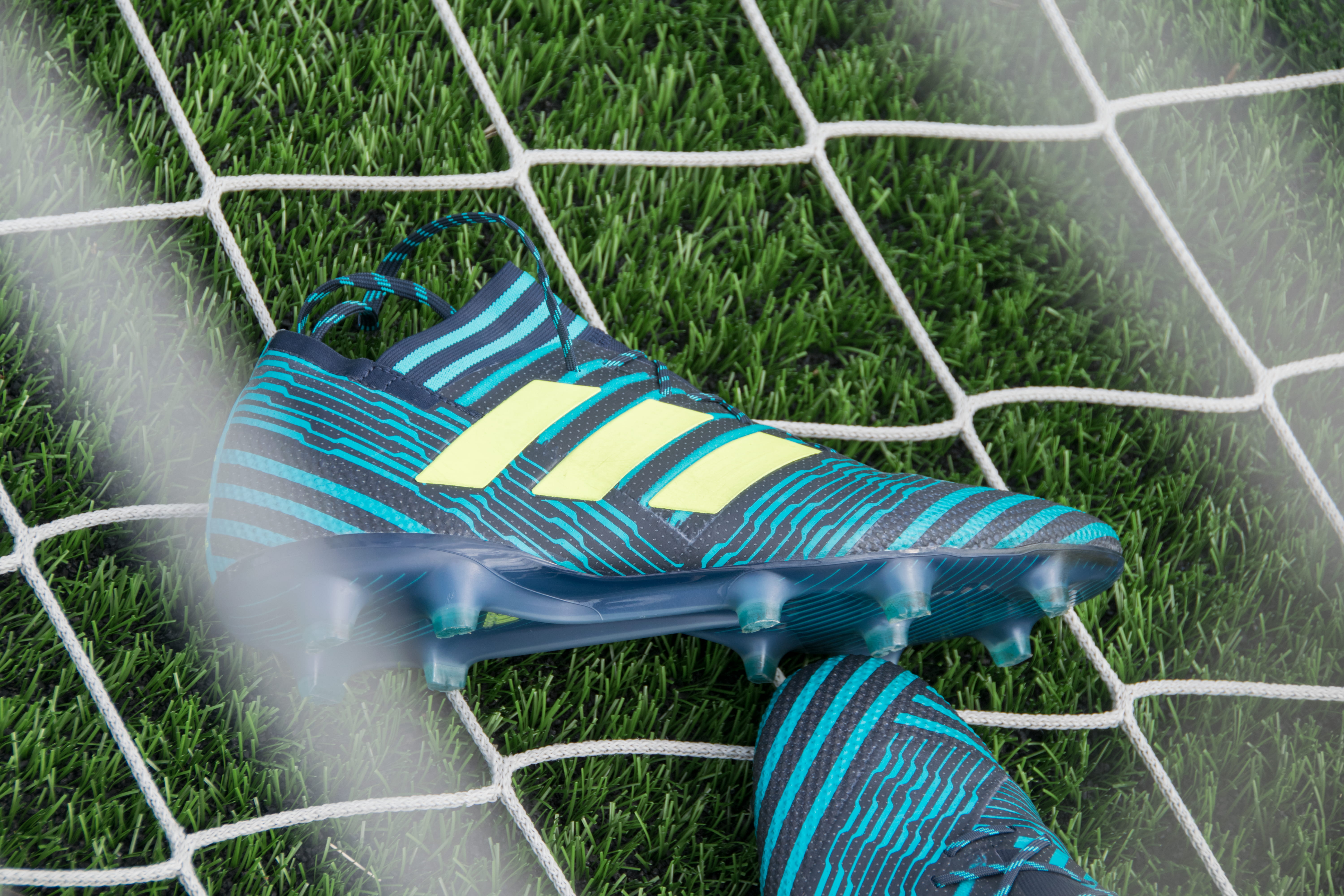 pair of blue-black-and-beige Adidas cleats, pair of green-and-black adidas cleats on white net