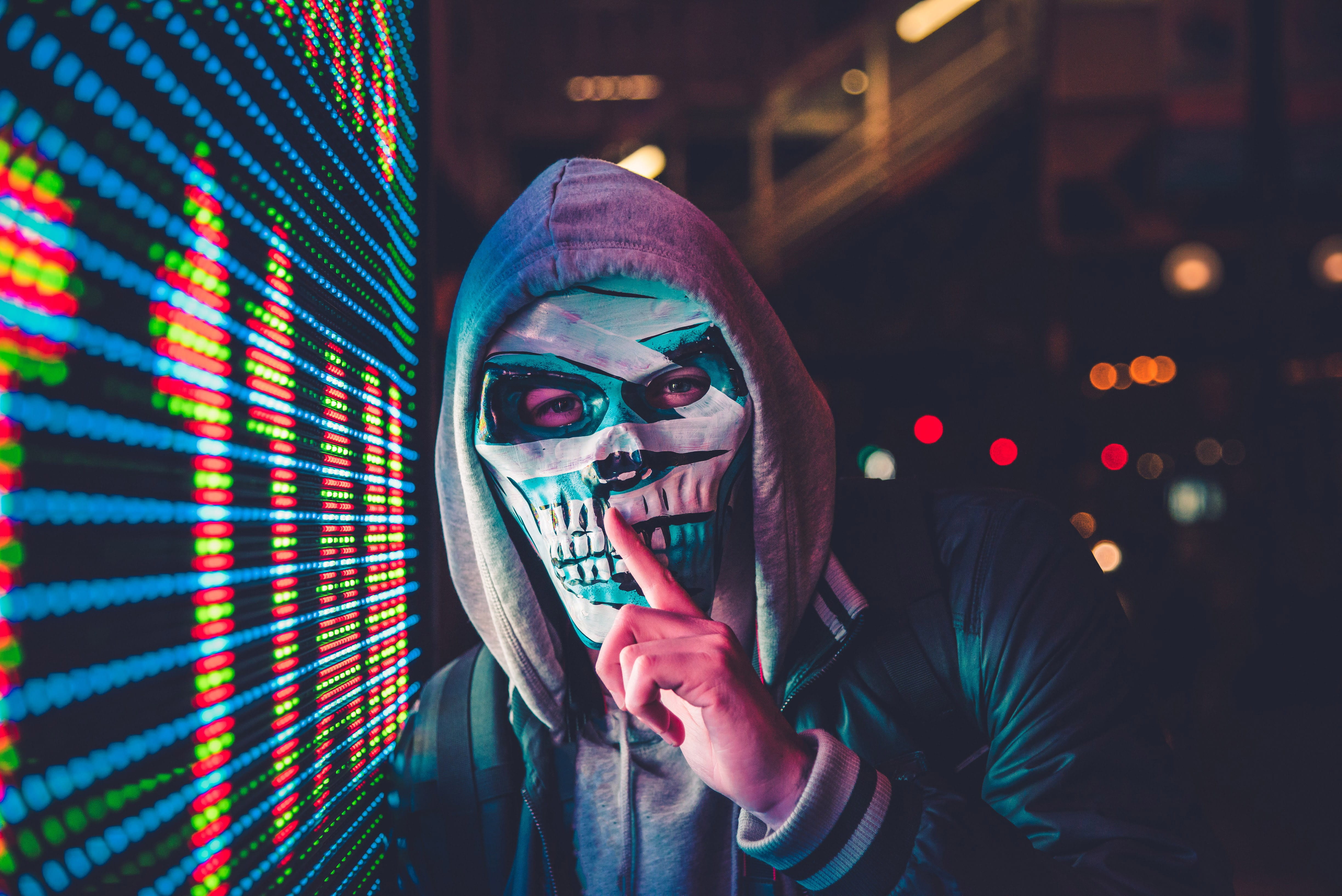person standing near LED sign, person wearing skull mask and hooded jacket