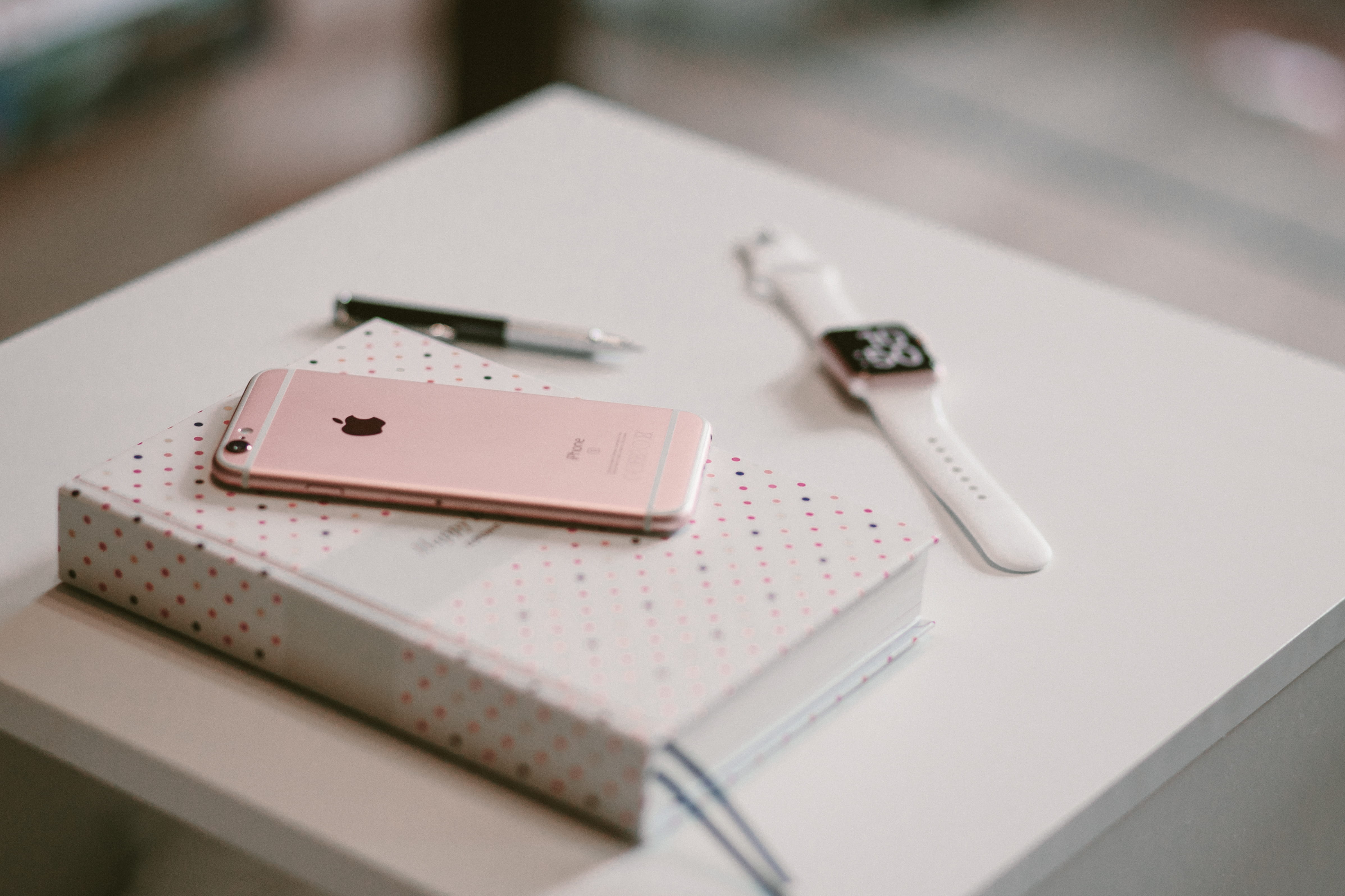 rose gold iPhone 6s on book near Apple watch, rose gold iPhone 6s on white notebook near gold Apple Watch