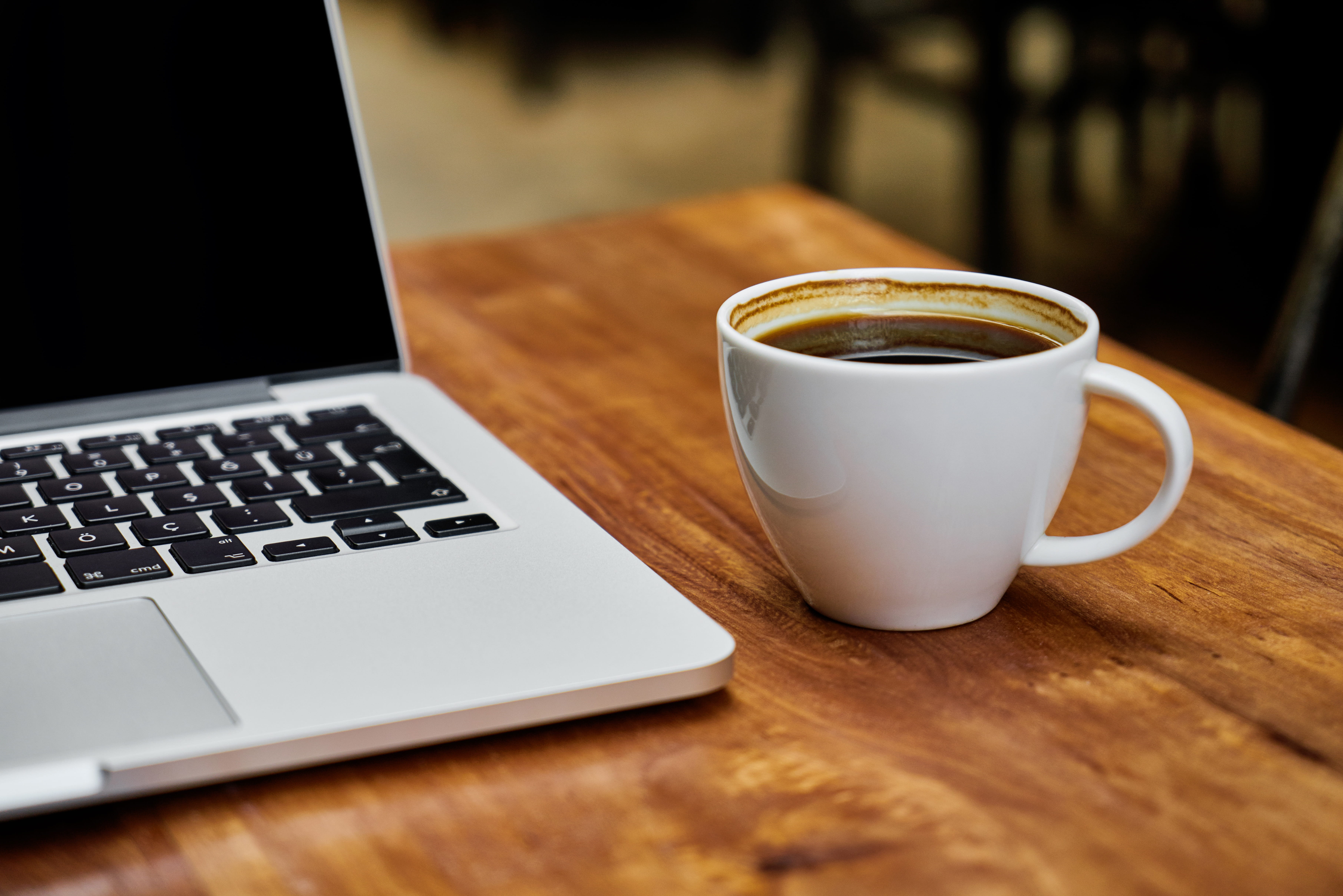 coffee filled white ceramic mug beside MacBook Pro on top of brown wooden table