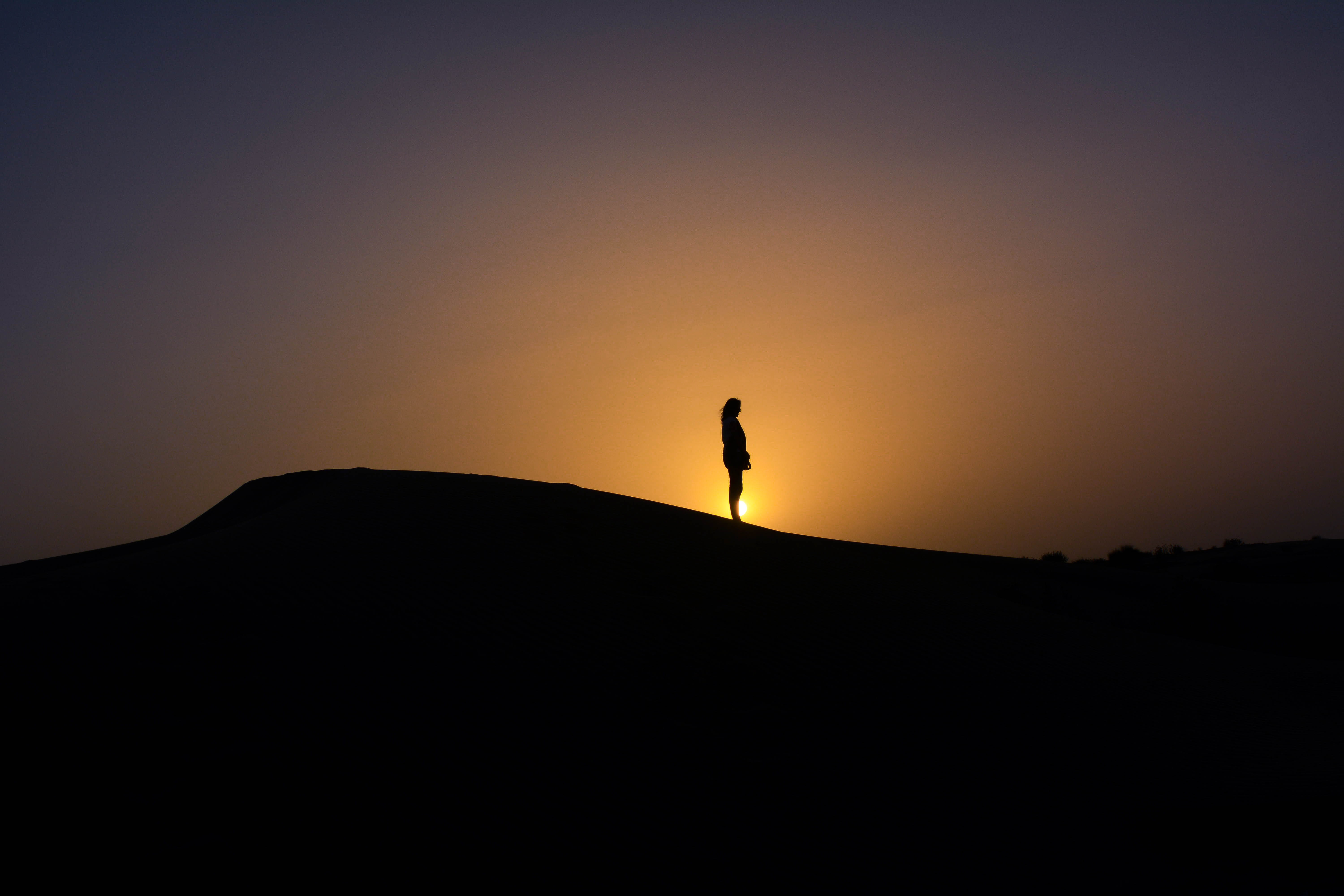 silhouette of person standing on mountain with sunset sun, silhouette of person standing on mound