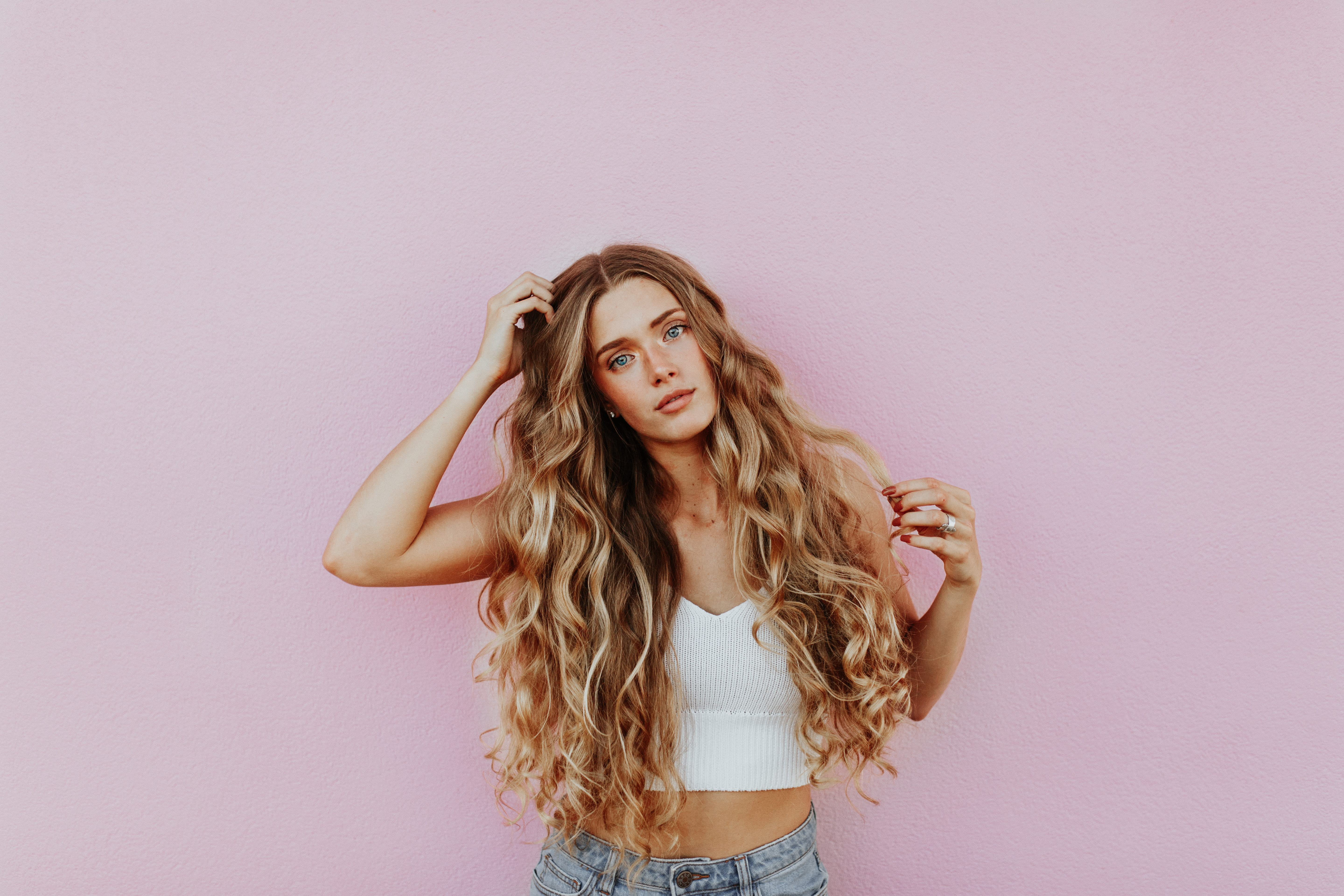 woman standing next to pink wall while scratching her head, woman touching her brown curly hair