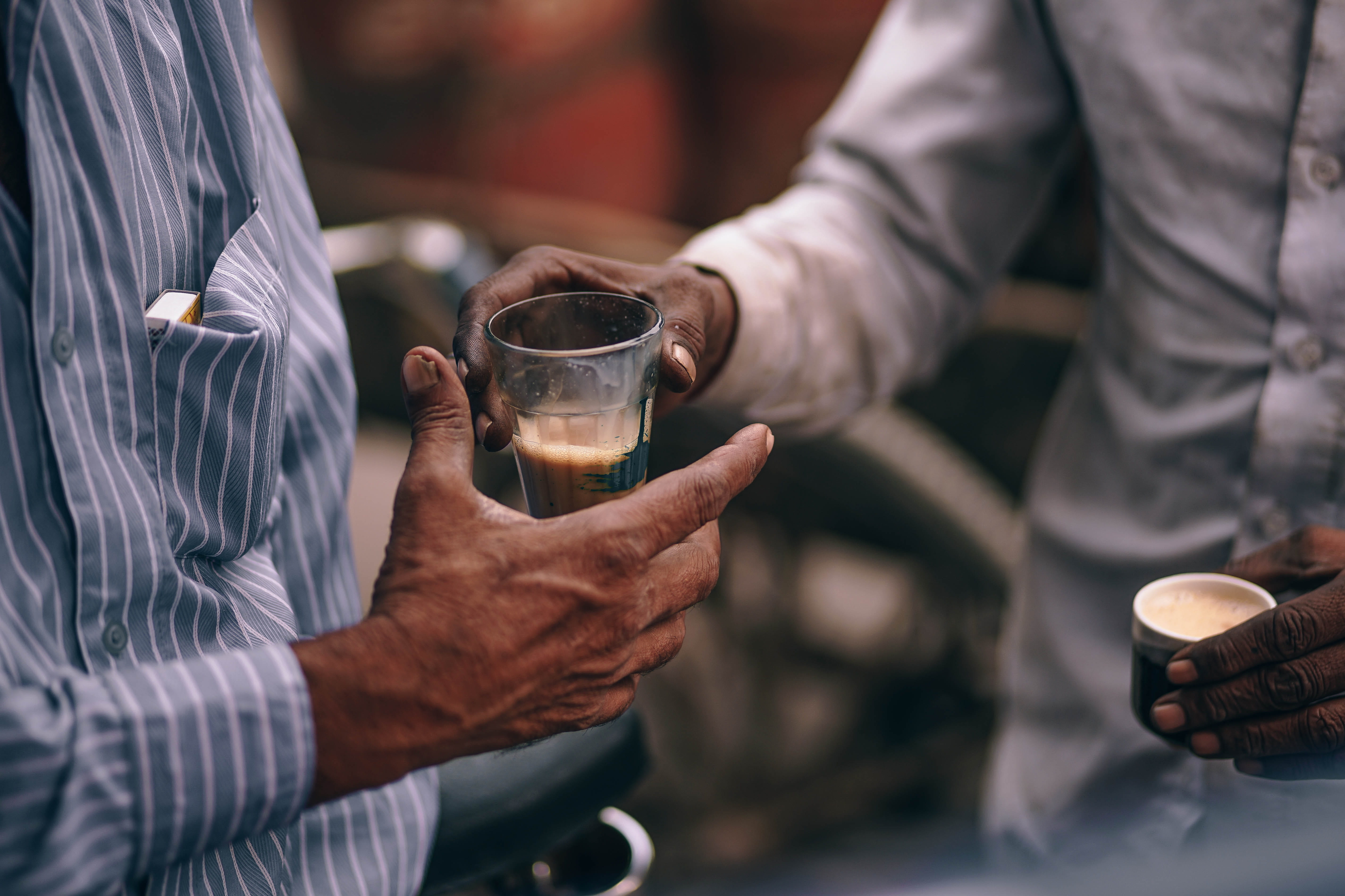 person handling drinking glass to a man, man about to give his drinking glass to man wearing white and blue striped dress shirt