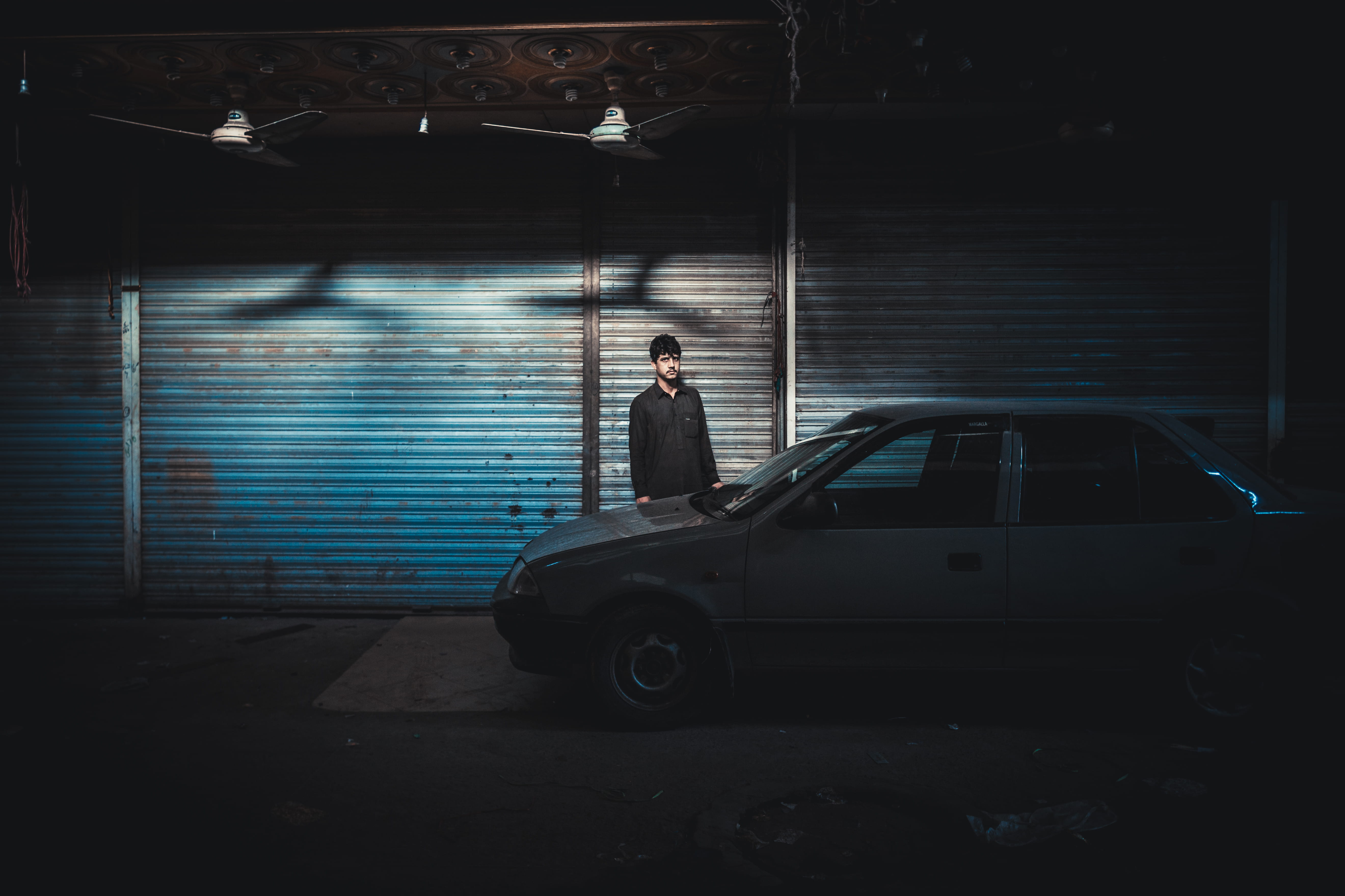 man near car, man standing in front of gray car parked across the street