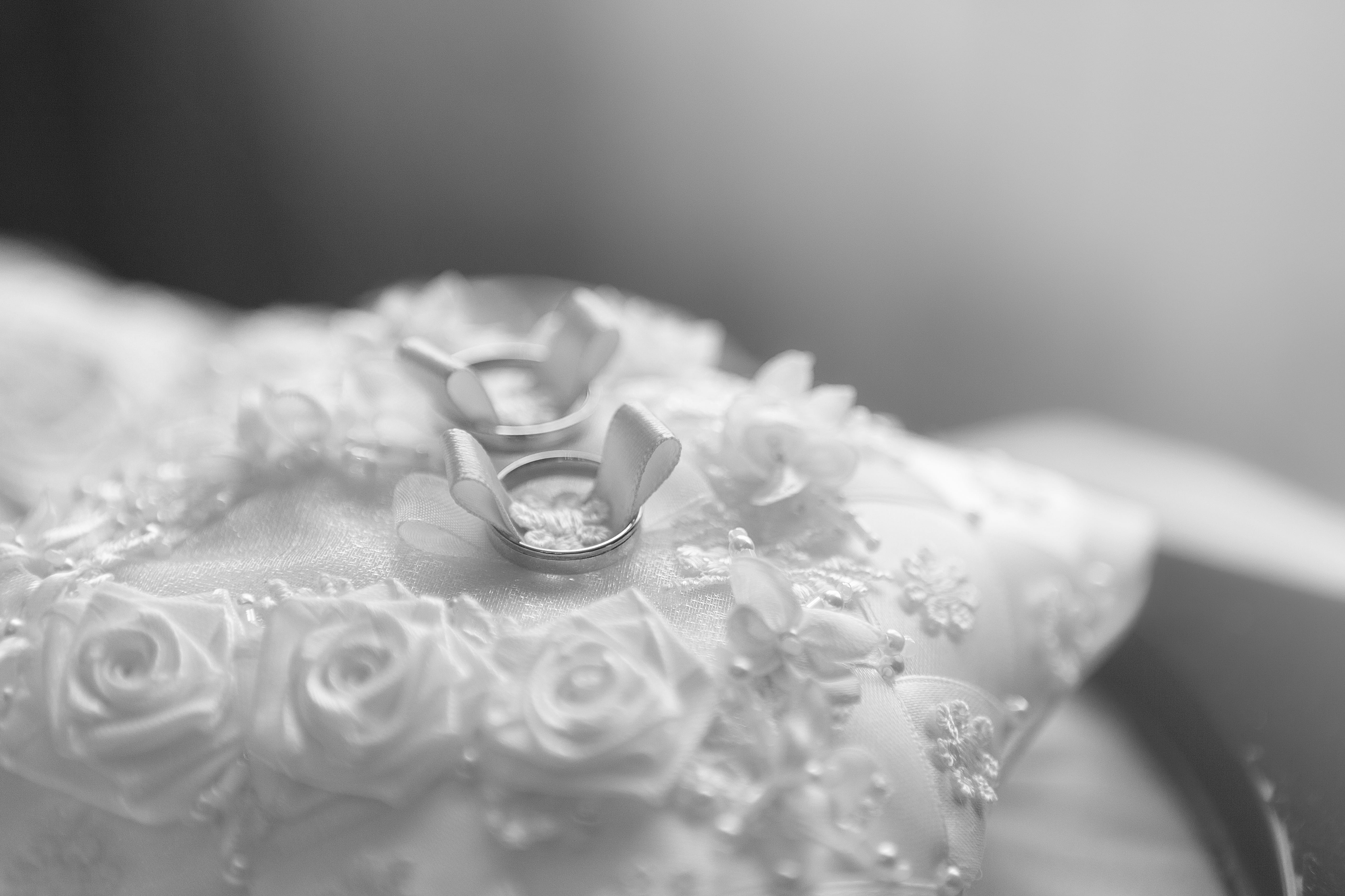 selective focus photo of silver-colored bridal ring on white lace pillow