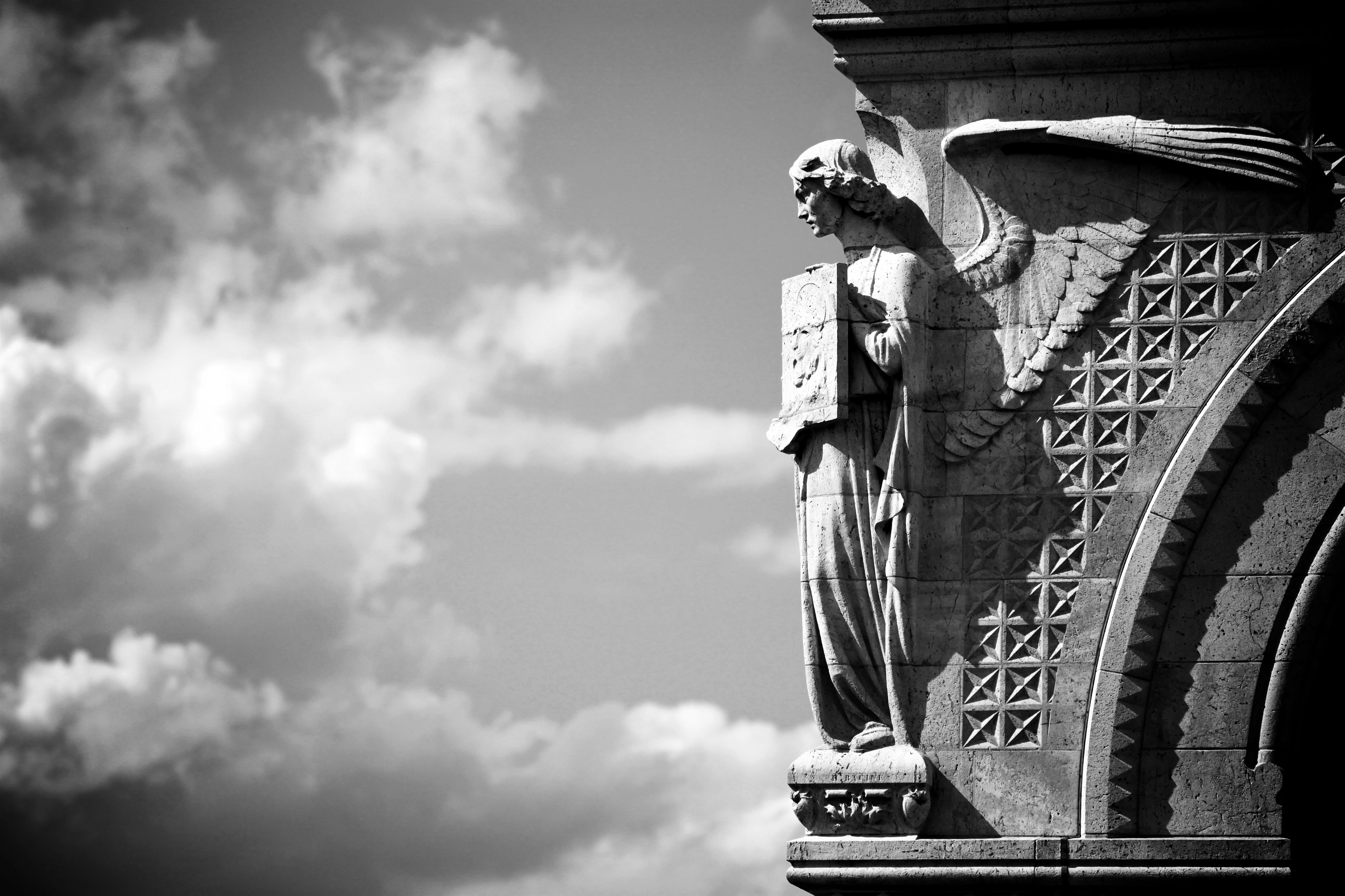 greyscale photo of angel statue sculpted on building, europe