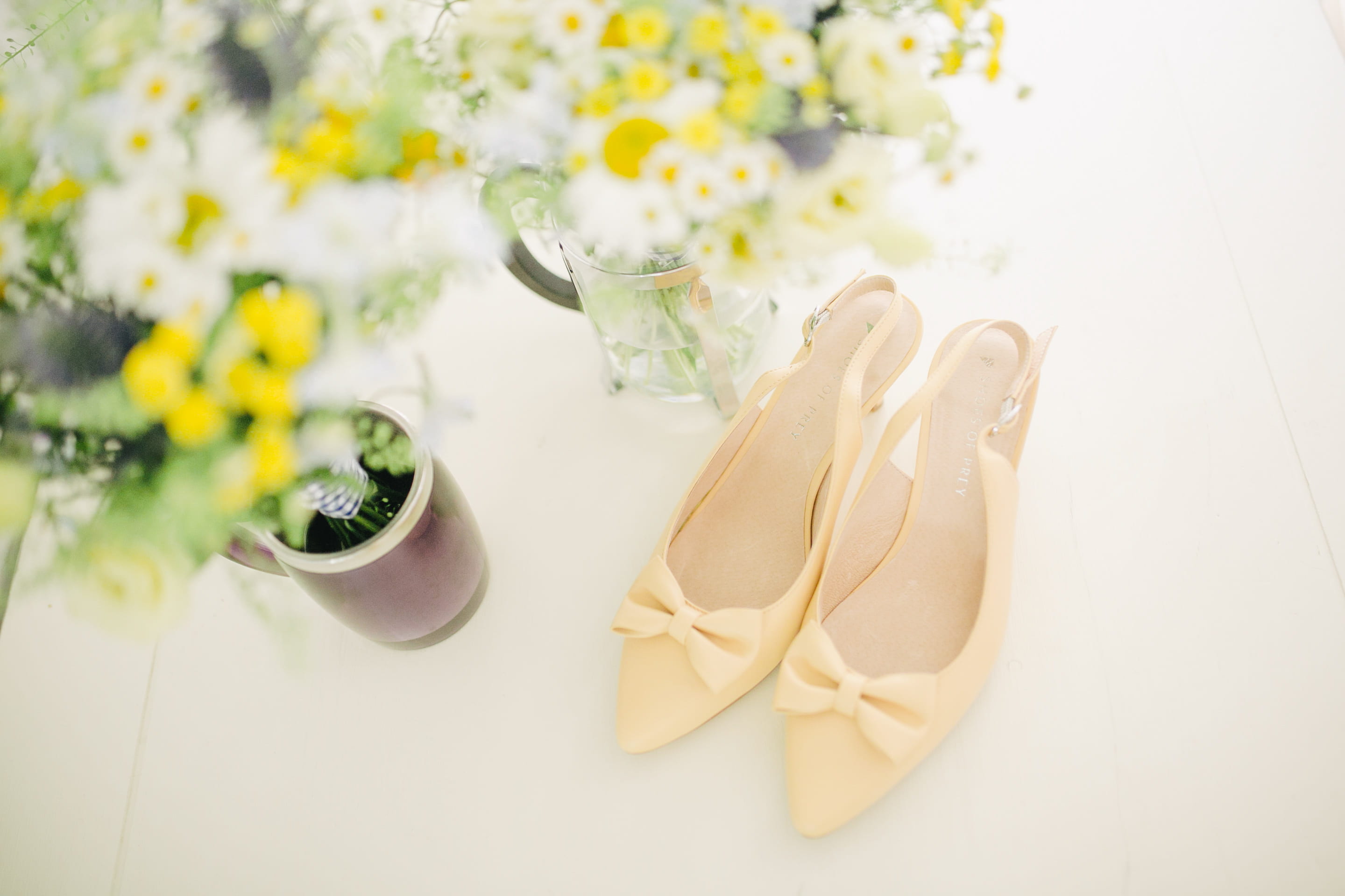 pair of women's beige pointed-toe slingback pumps with ribbons near flower vase, pair of yellow slingback strap stilettos