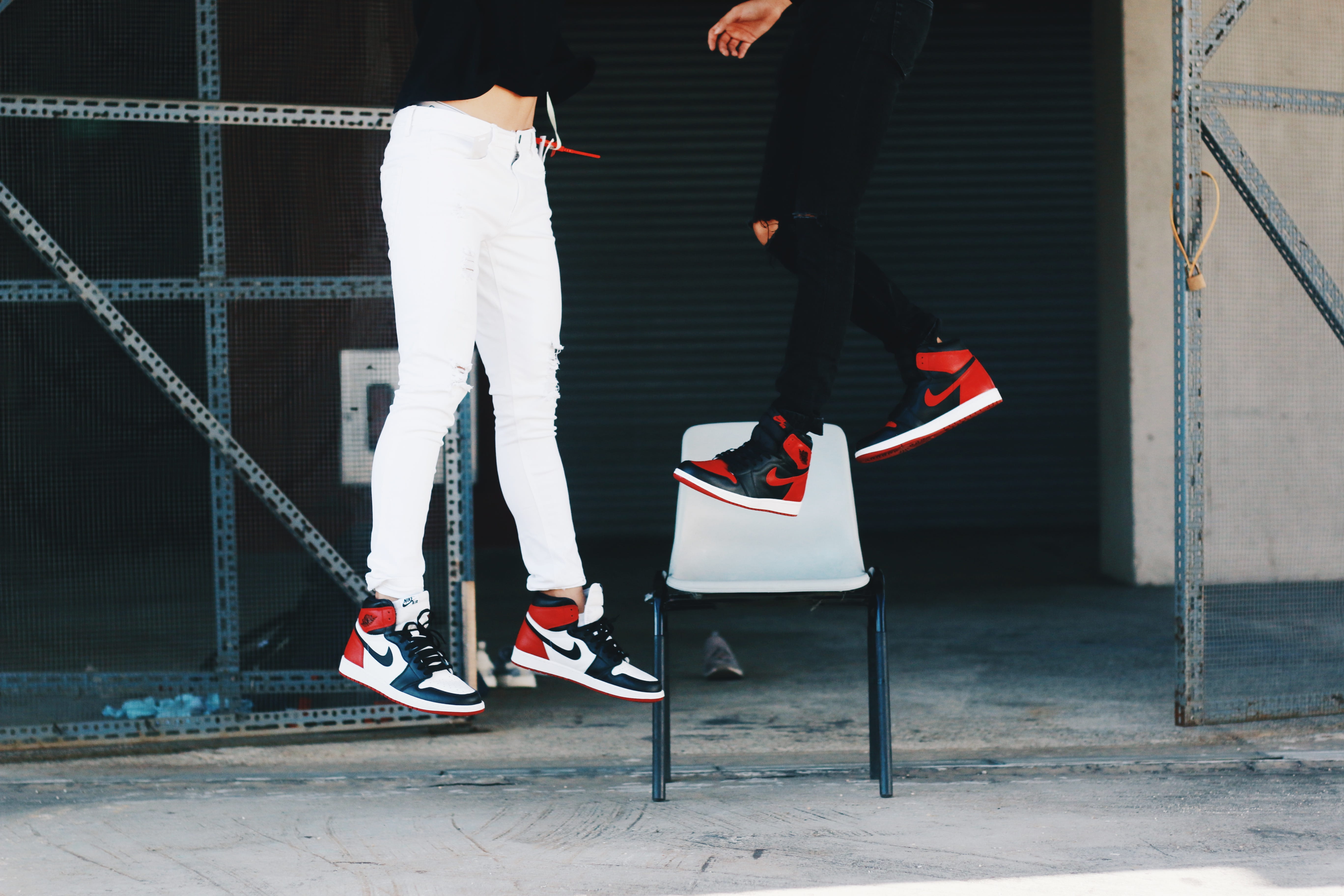 two people wearing Air Jordan shoes jumping, two person wearing black toe and bred Air Jordan 1 shoes floating on air