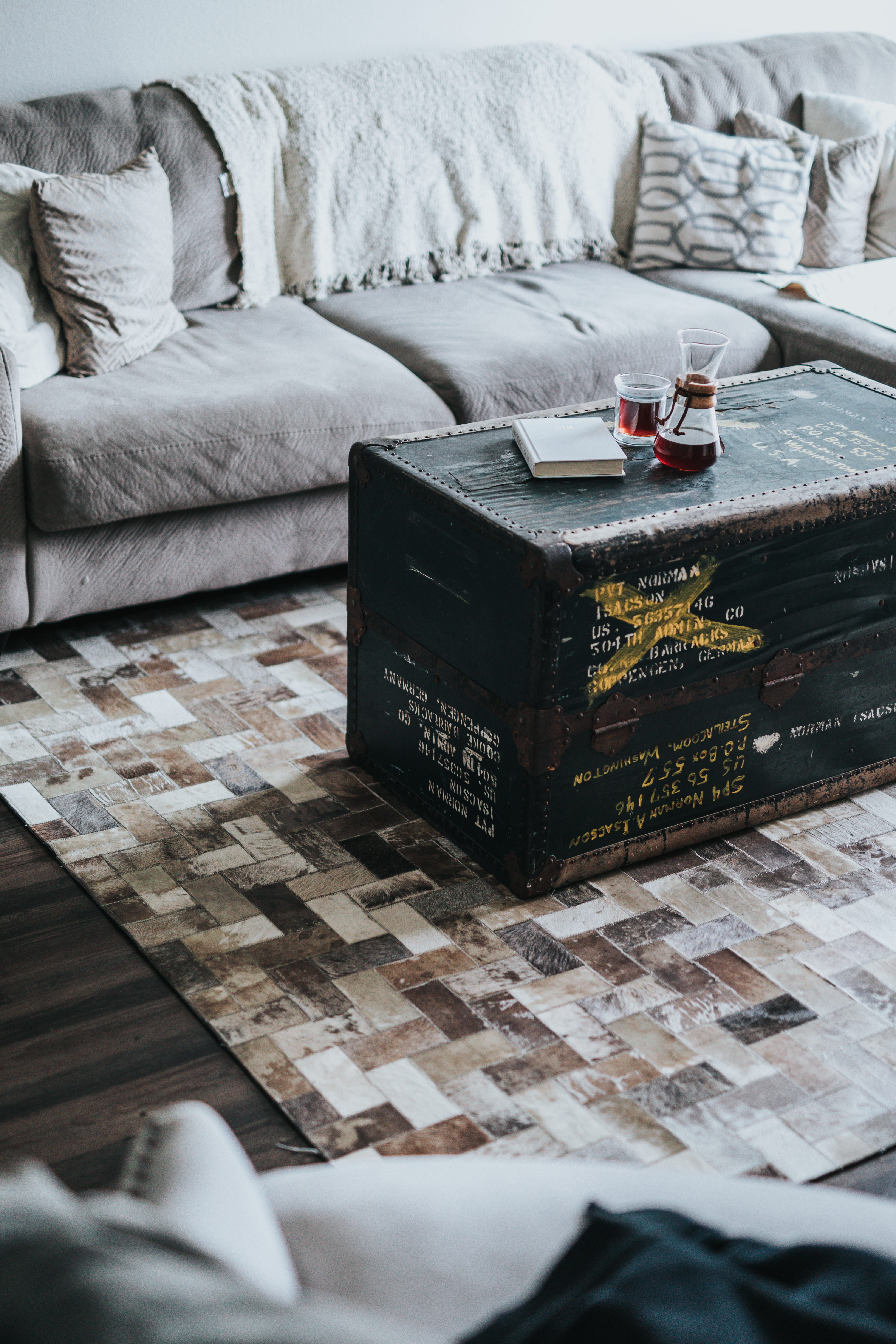 black ammo box coffee table between sofas, rectangular black wicker table beside gray sofa