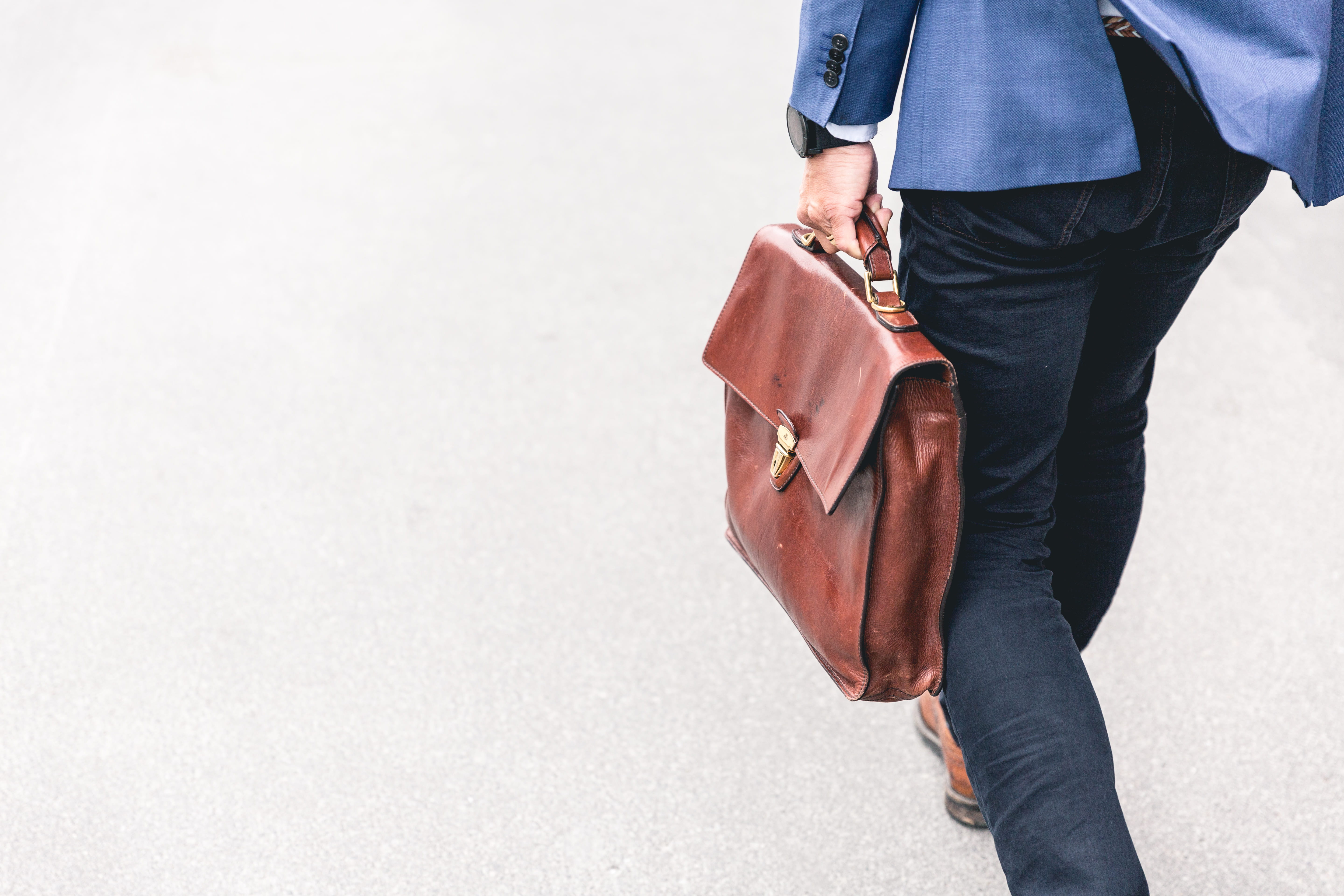 person walking holding brown leather bag, man in blue suit jacket and black pants holding leather bag