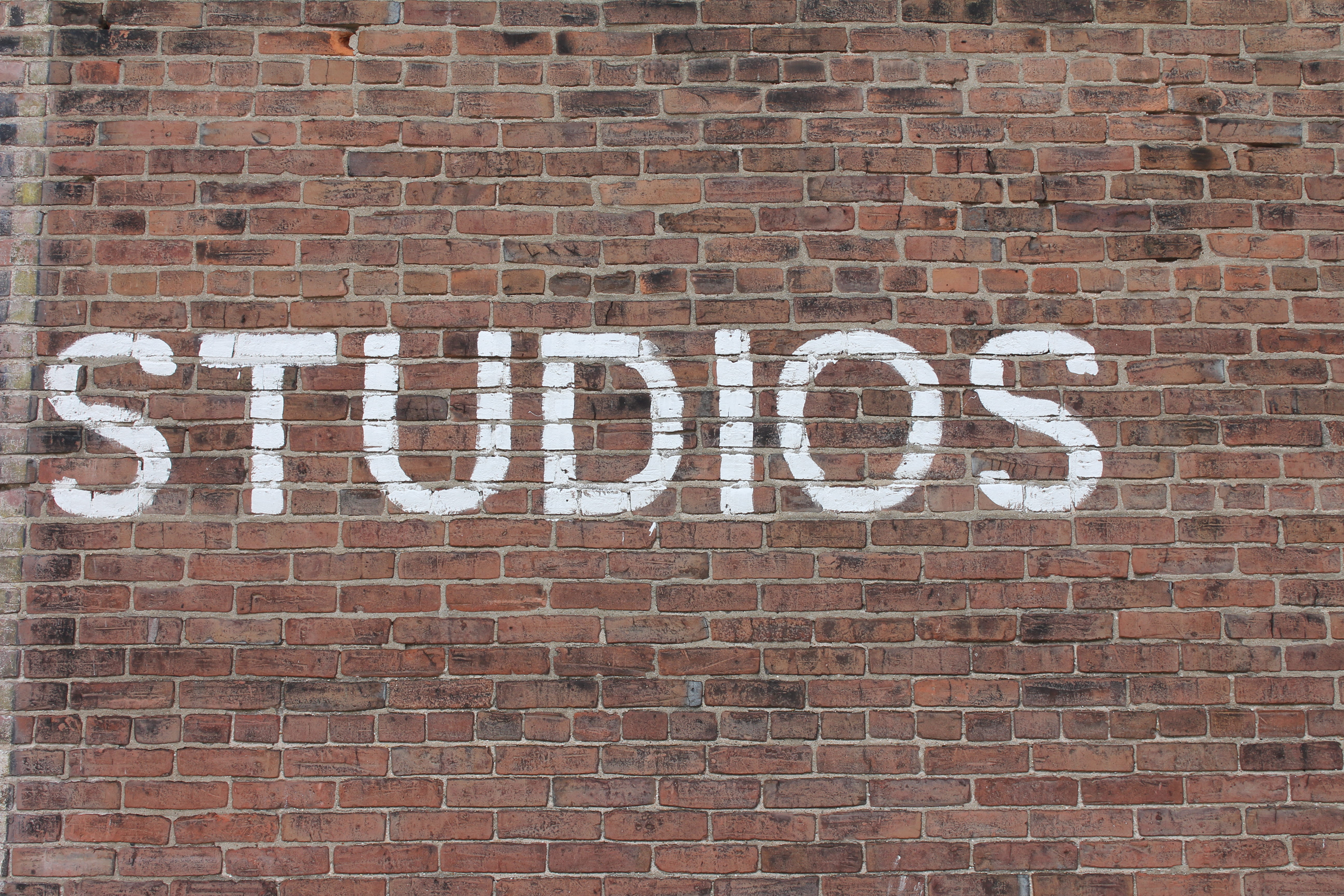Studios text on brown brick wall, Studios print on brick wall
