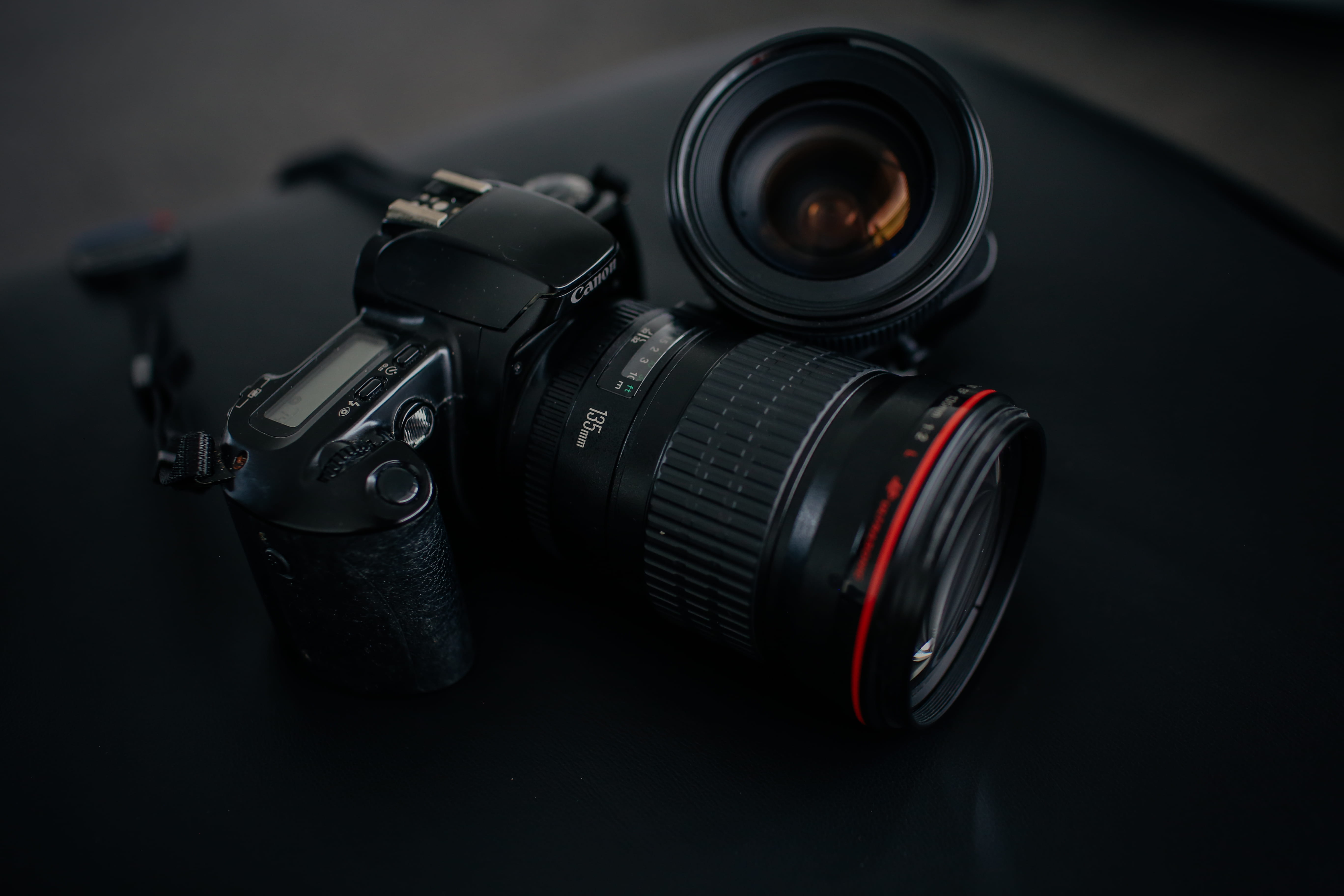 black Canon DSLR camera beside camera lens, black camera lens leaning on DSLR camera