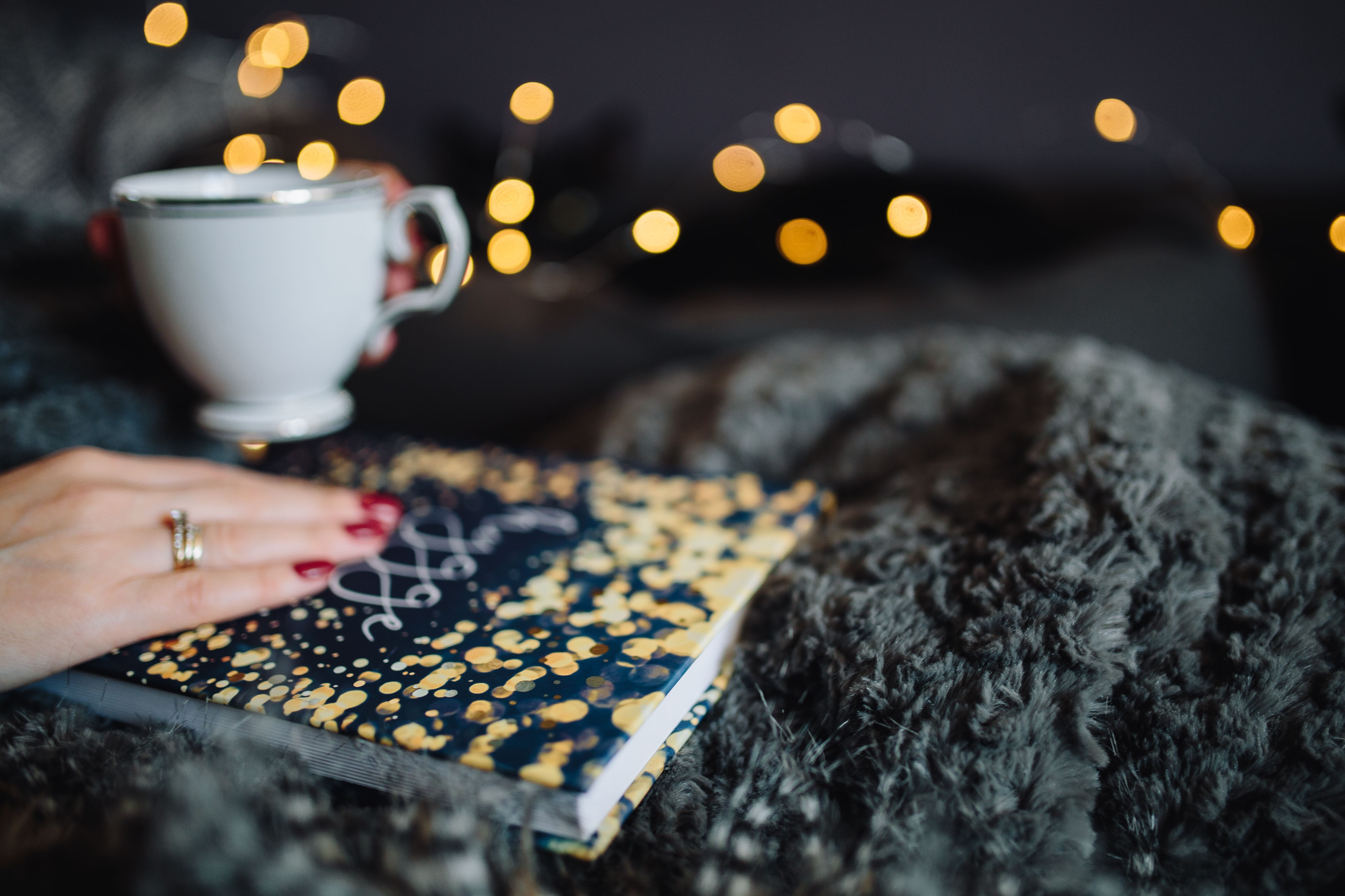 Young woman at home reading Hygge book and drinking, indoor, femine