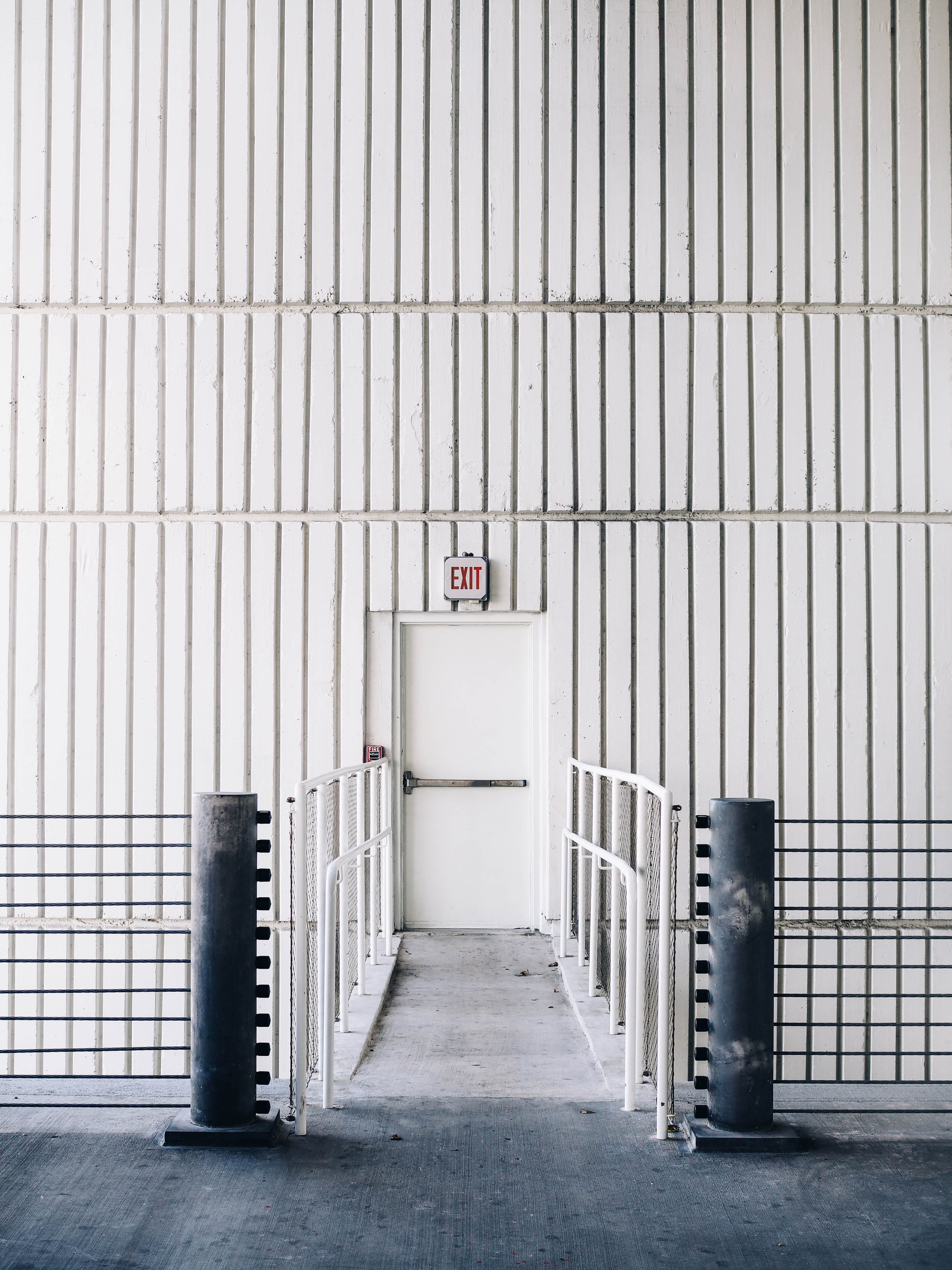 architectural photography of exit door with bridge, gray concrete foot bridge leading to exit inside the building