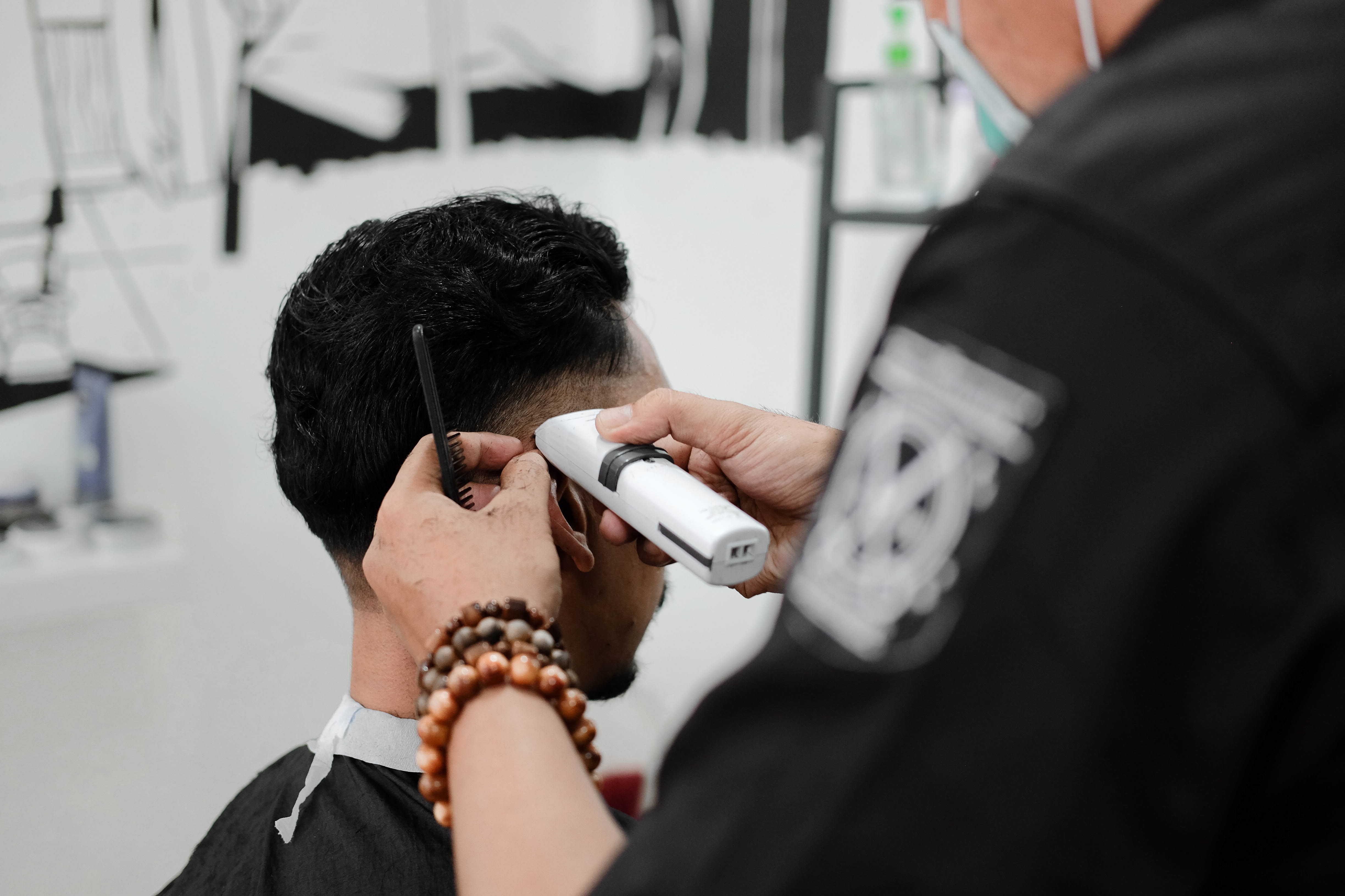 man holding white hair trimmer, man razoring another man's hair