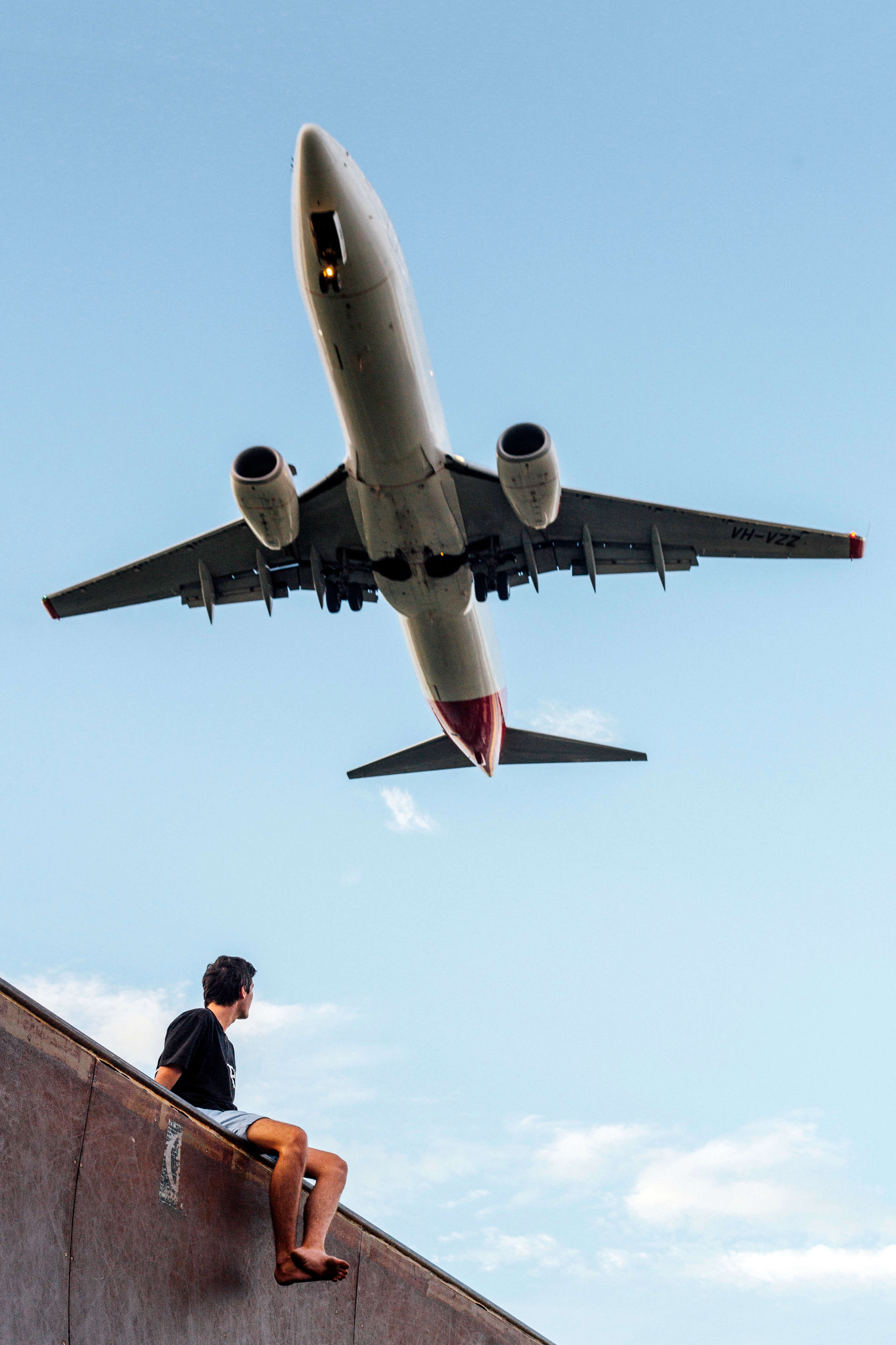 low angle photography of man wearing black shirt under white and gray airplane, man sitting under airplane