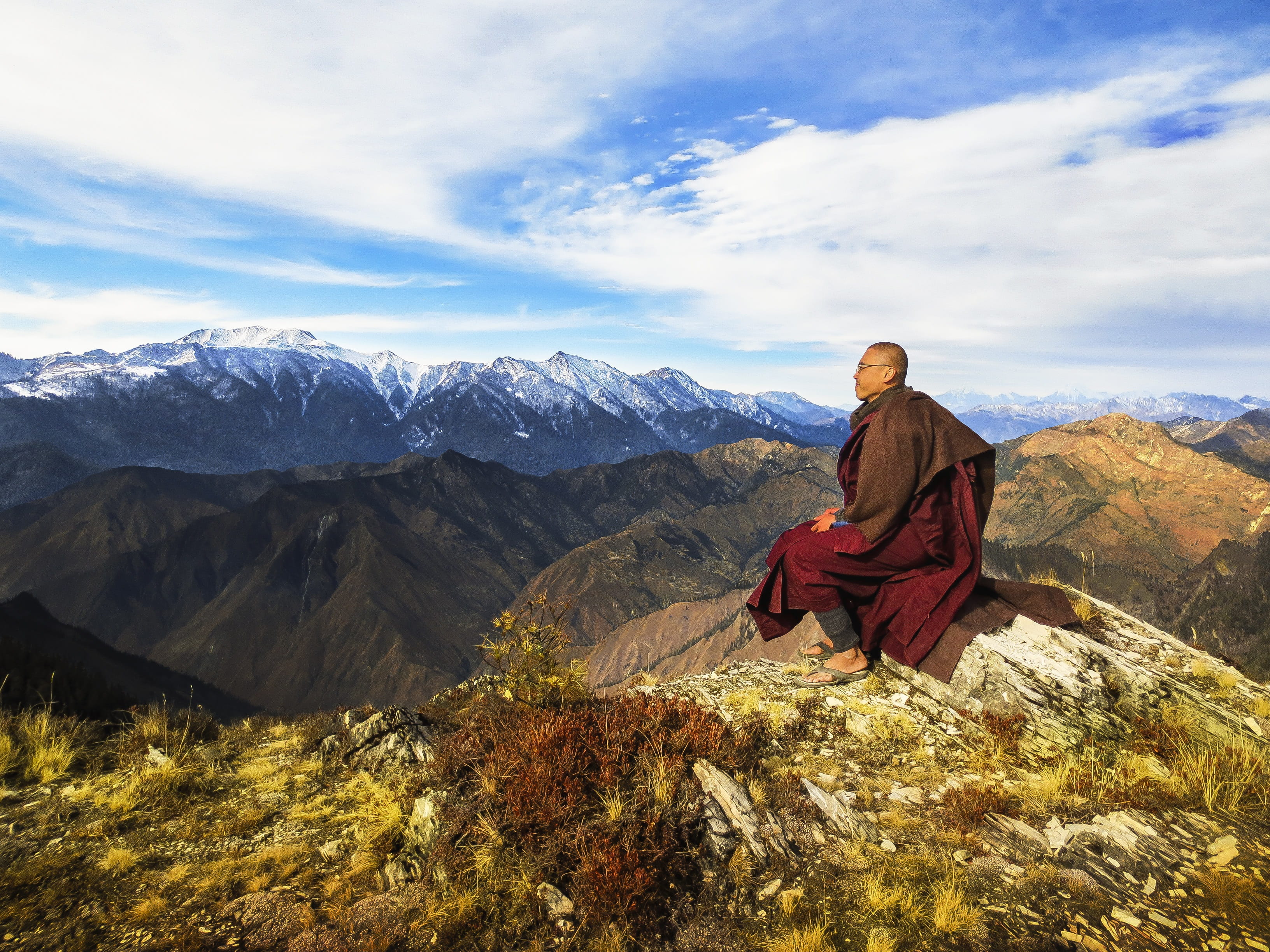 monk sitting on the cliff on the mountain under the blue sky during daytime