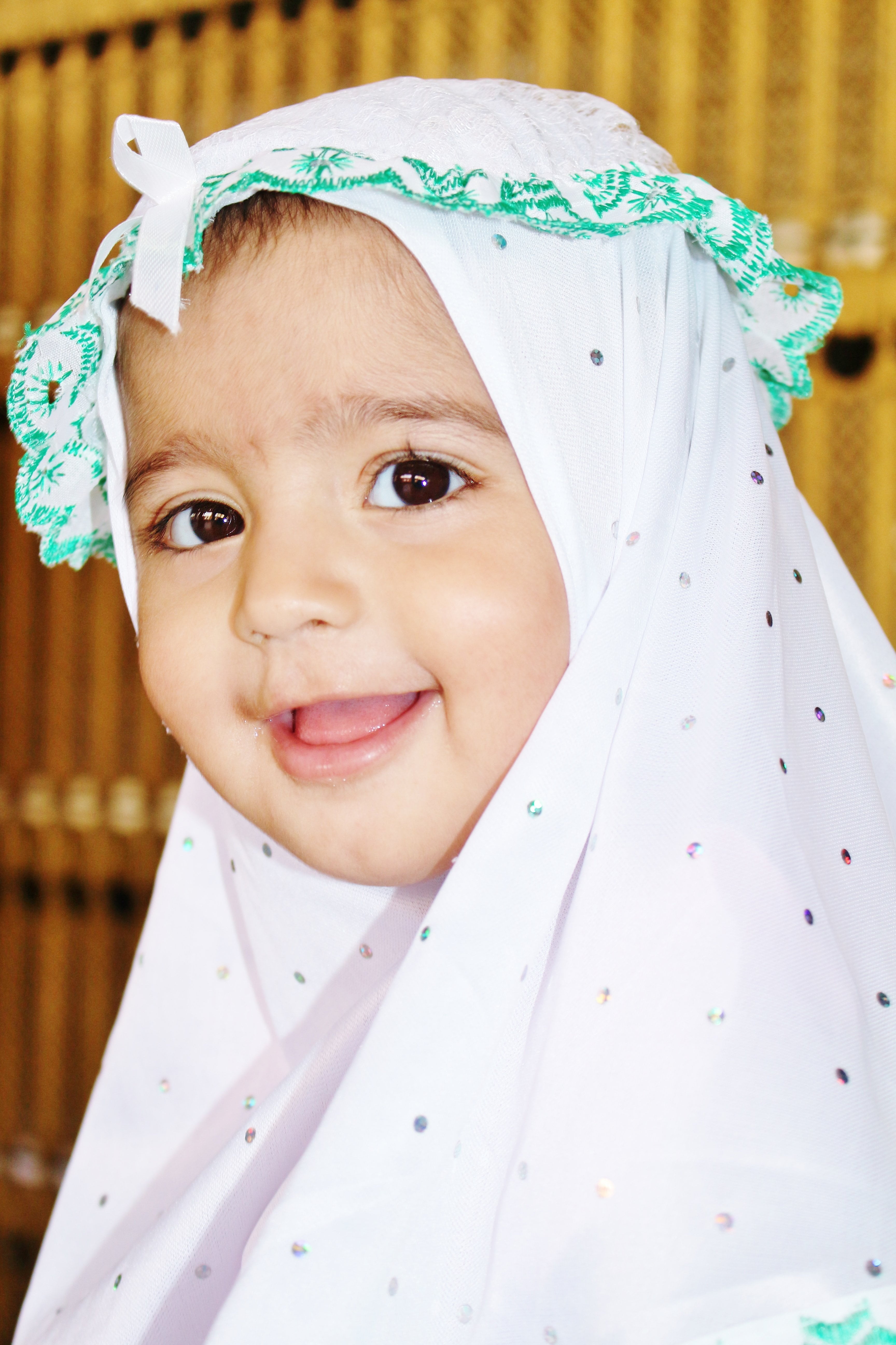smiling baby wearing white and black polka-dot headdress, muslim