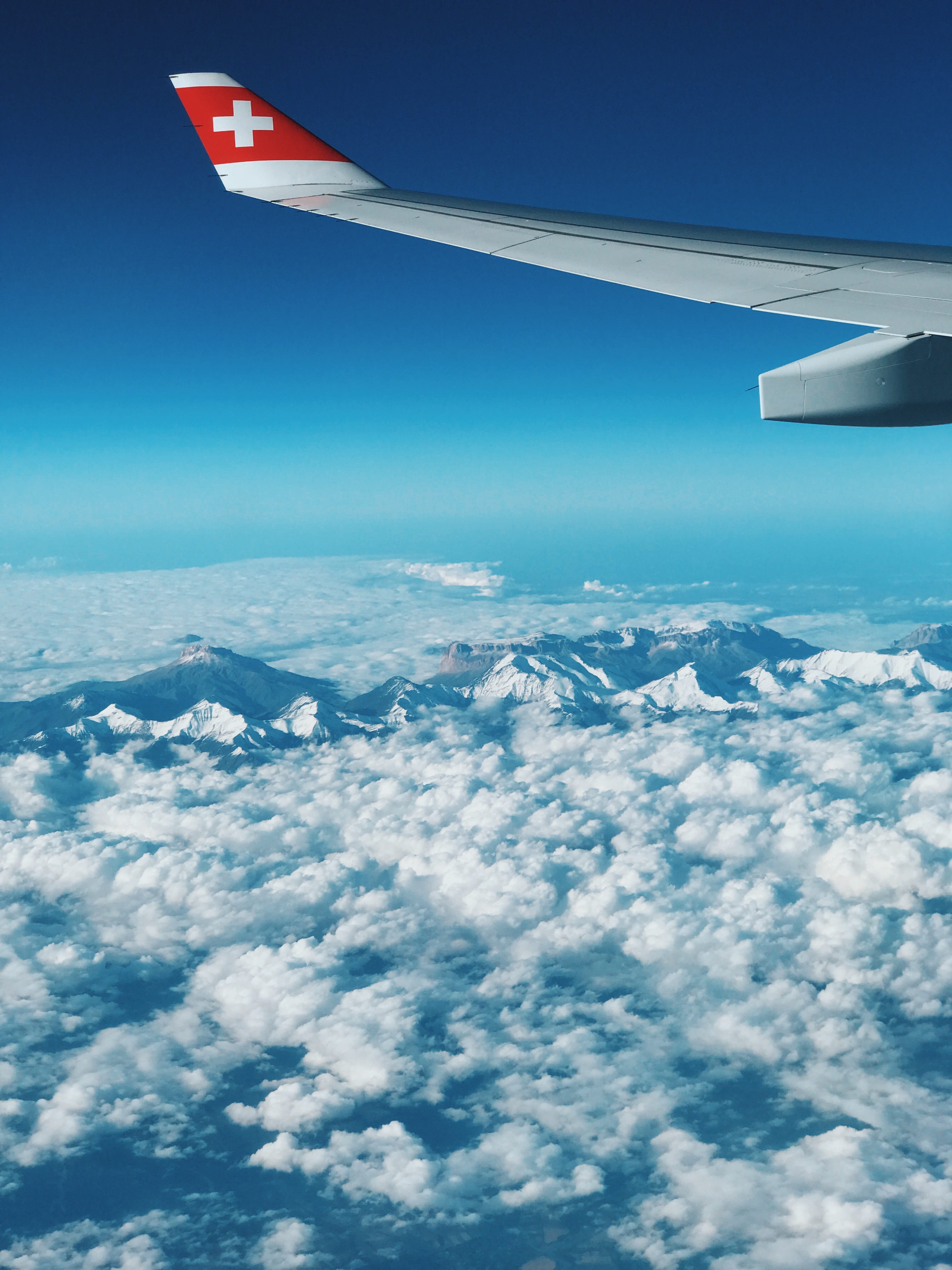 Flying  from Switzerland, gray airplane wing above white clouds