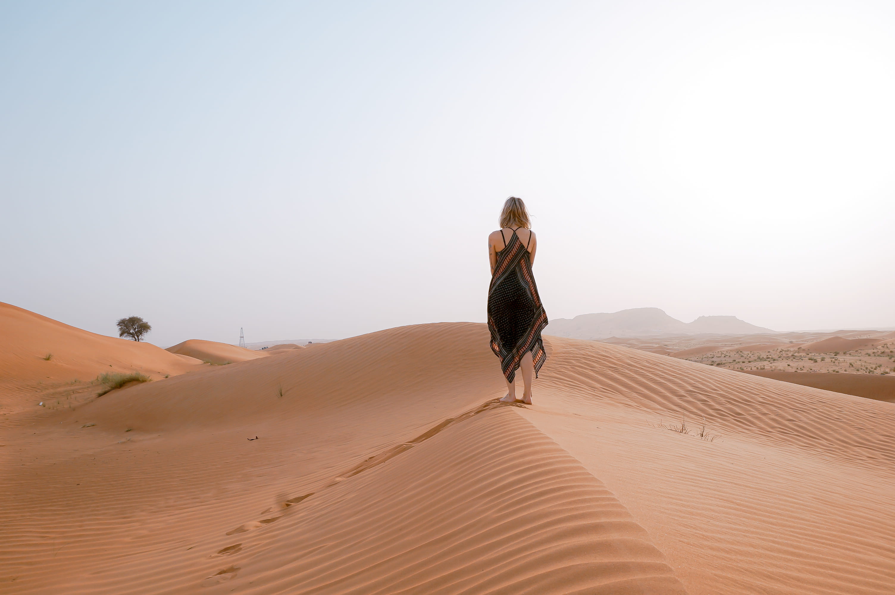 woman walking on desert during daytime, woman stands on brown sand