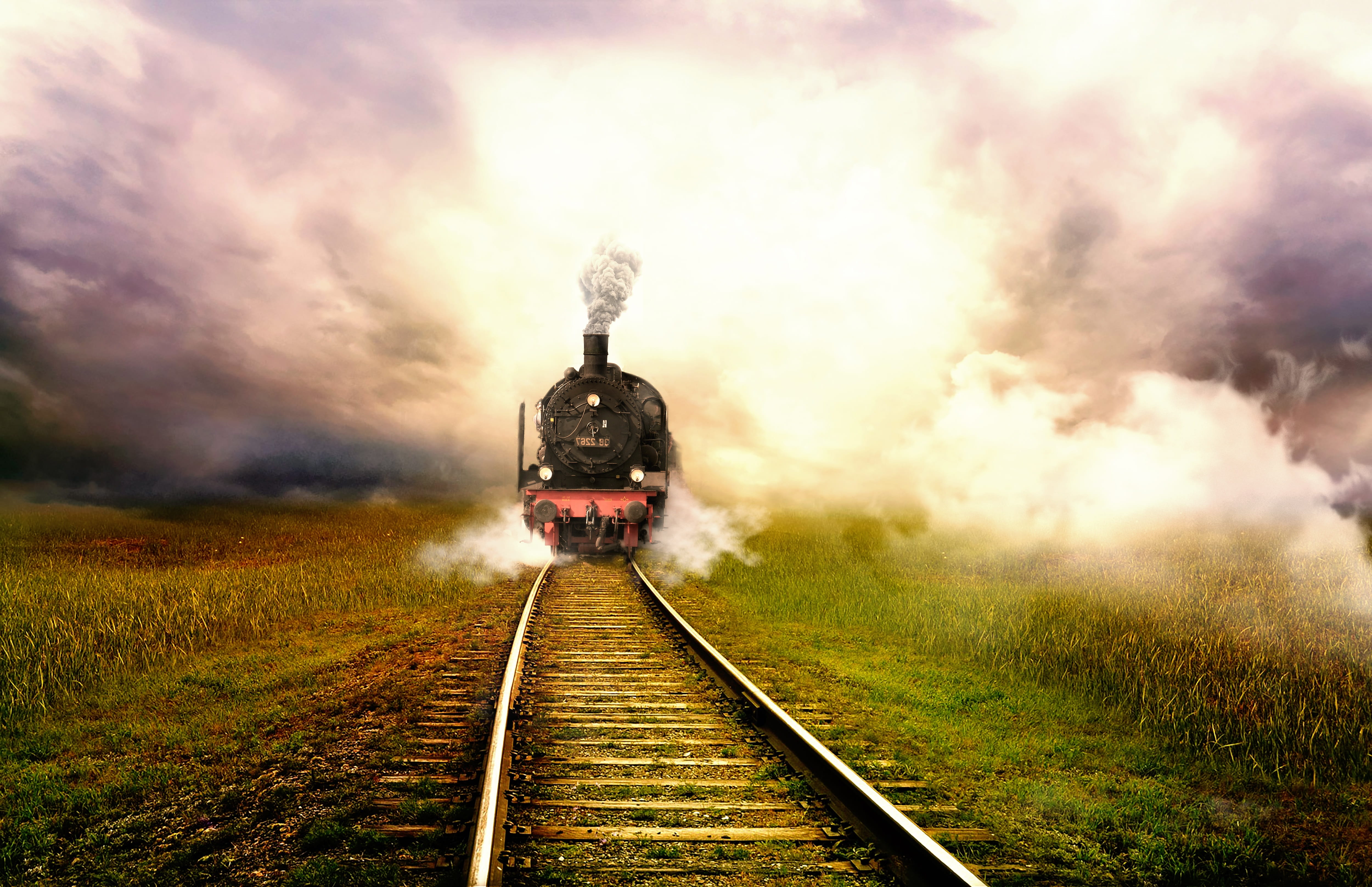 steam engine train travelling on  track under white clouds, landscape