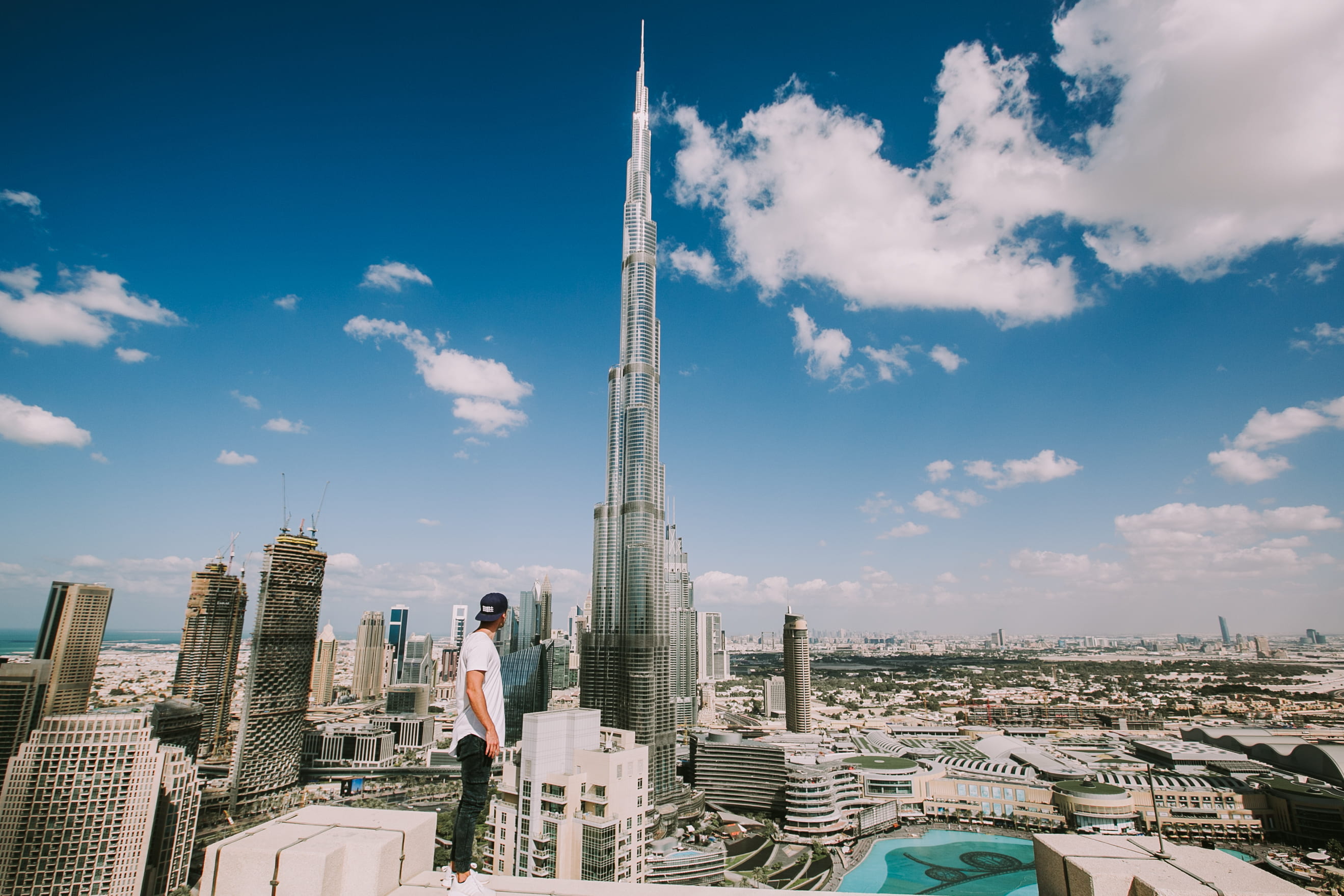 Burj Khalifa, Dubai during daytime, man standing alone on top of building looking at the city's tallest building during daytime