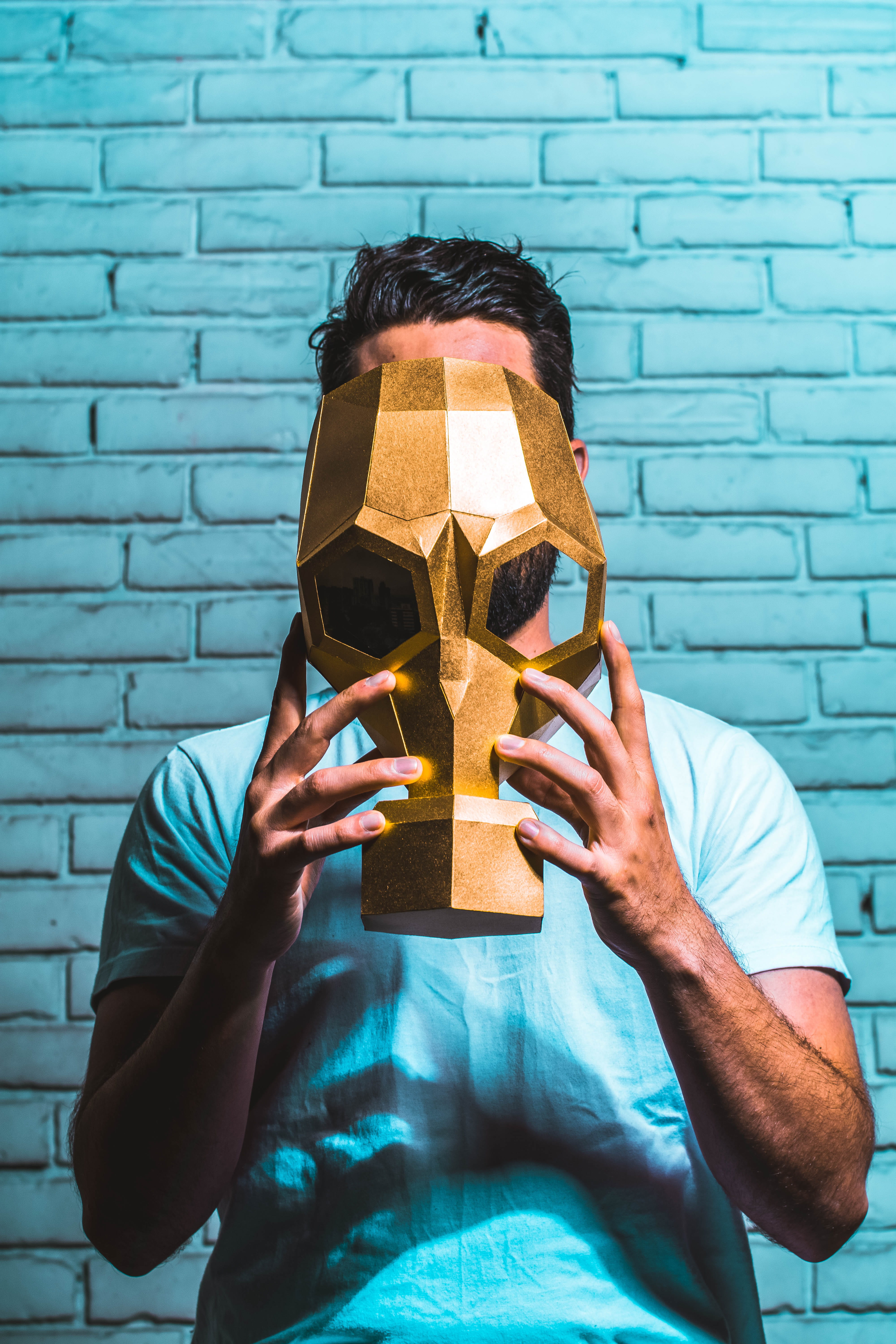 man holding a mask with gold paint, person standing in front wall holding mask