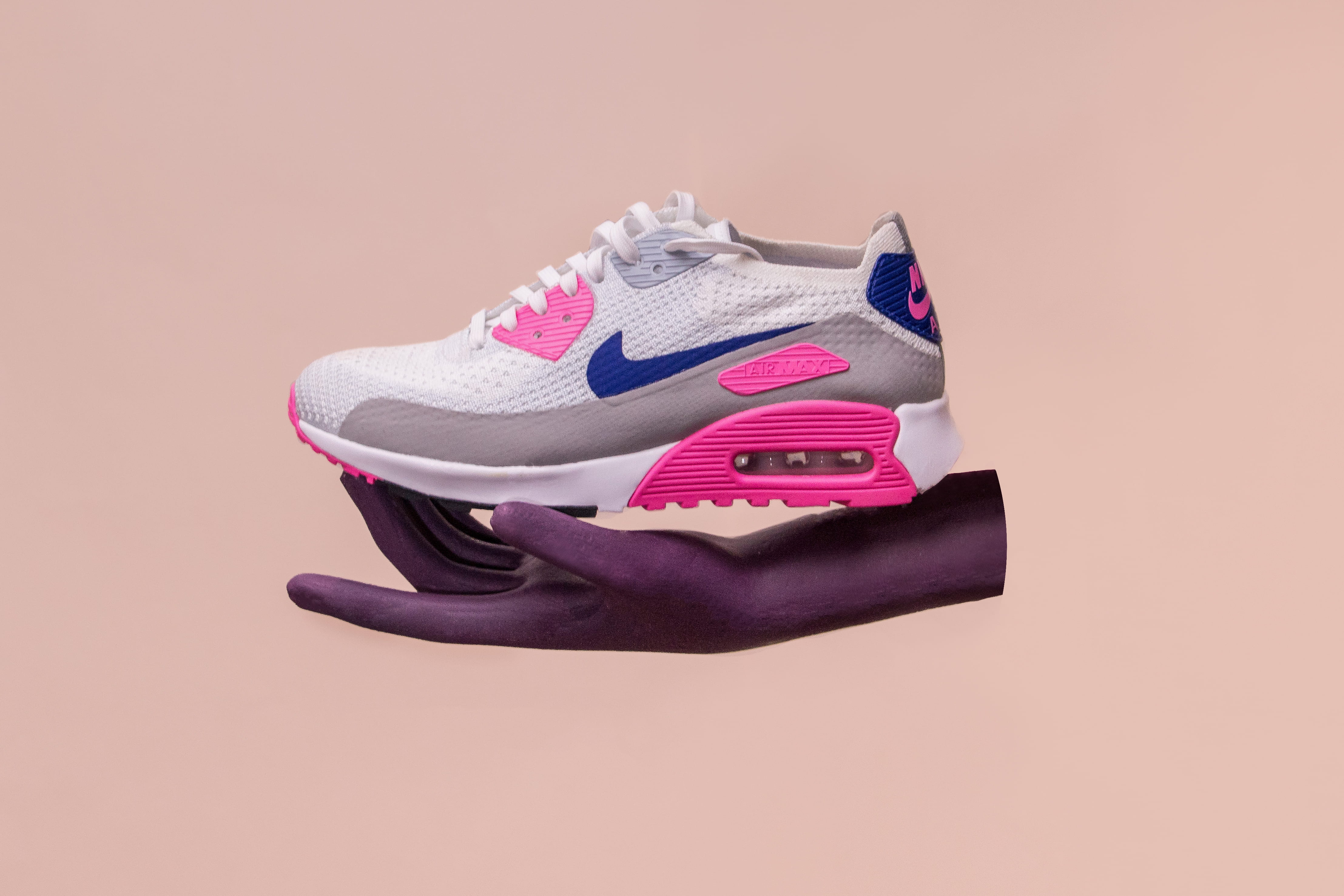unpaired white, gray, and blue Nike Air Max 90 shoe, white, pink, and brown Nike Air Max 90 on person's hand