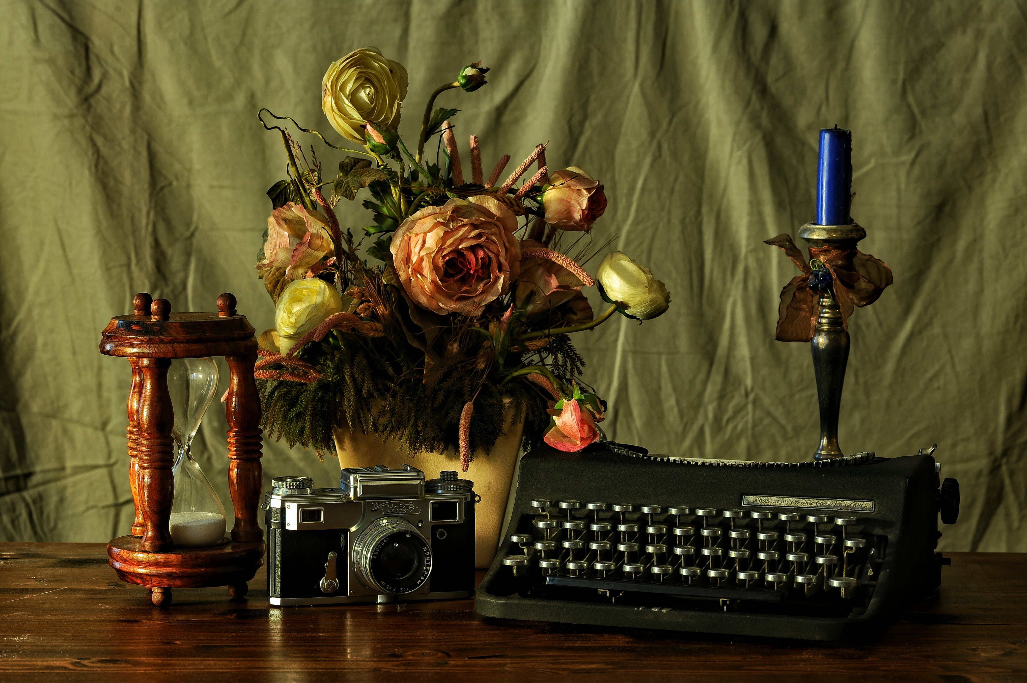 typewriter beside camera, hourglass, flower decor, and candlestick with candle on table