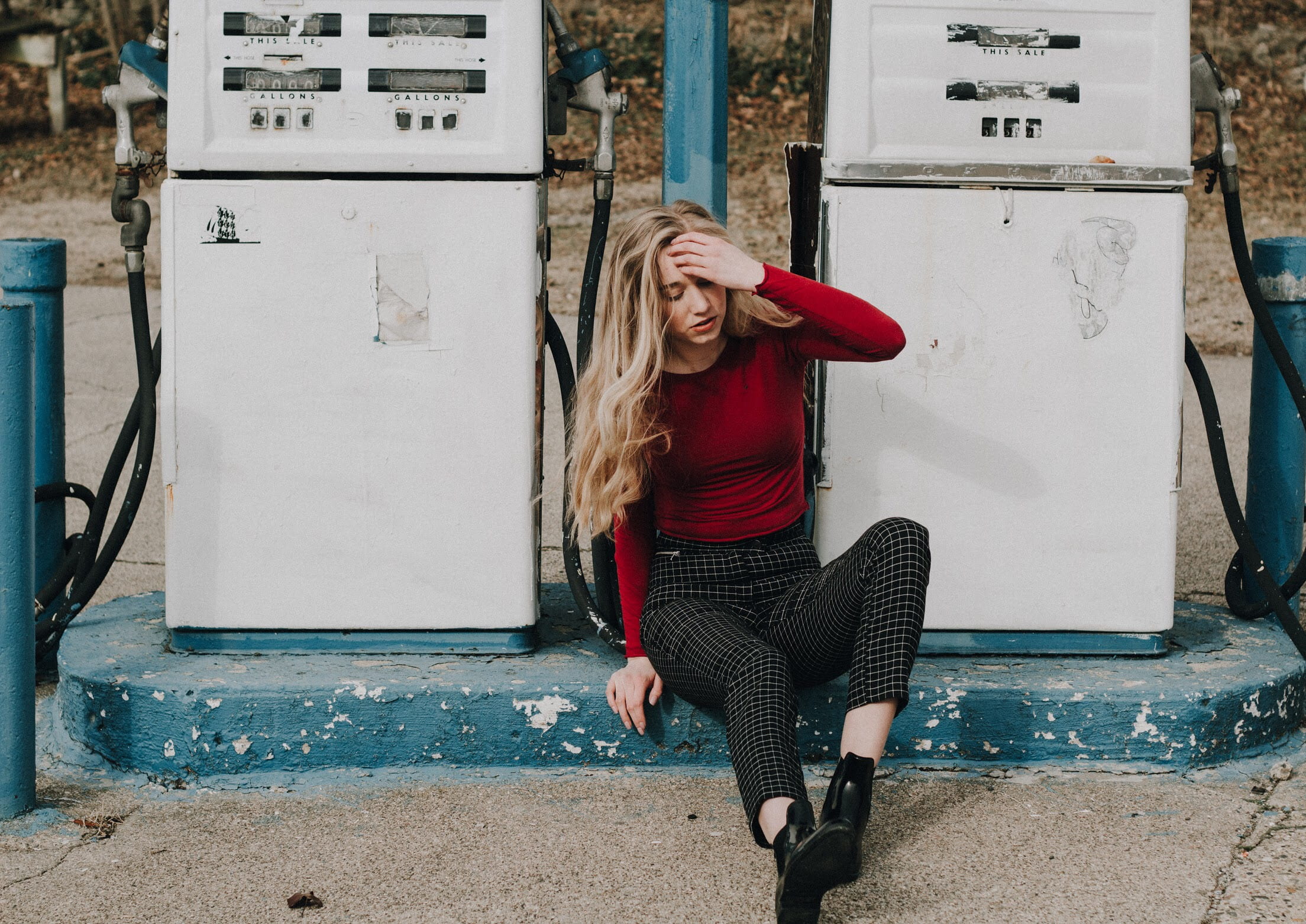 woman sits between two white gas pumps, woman sitting on ground