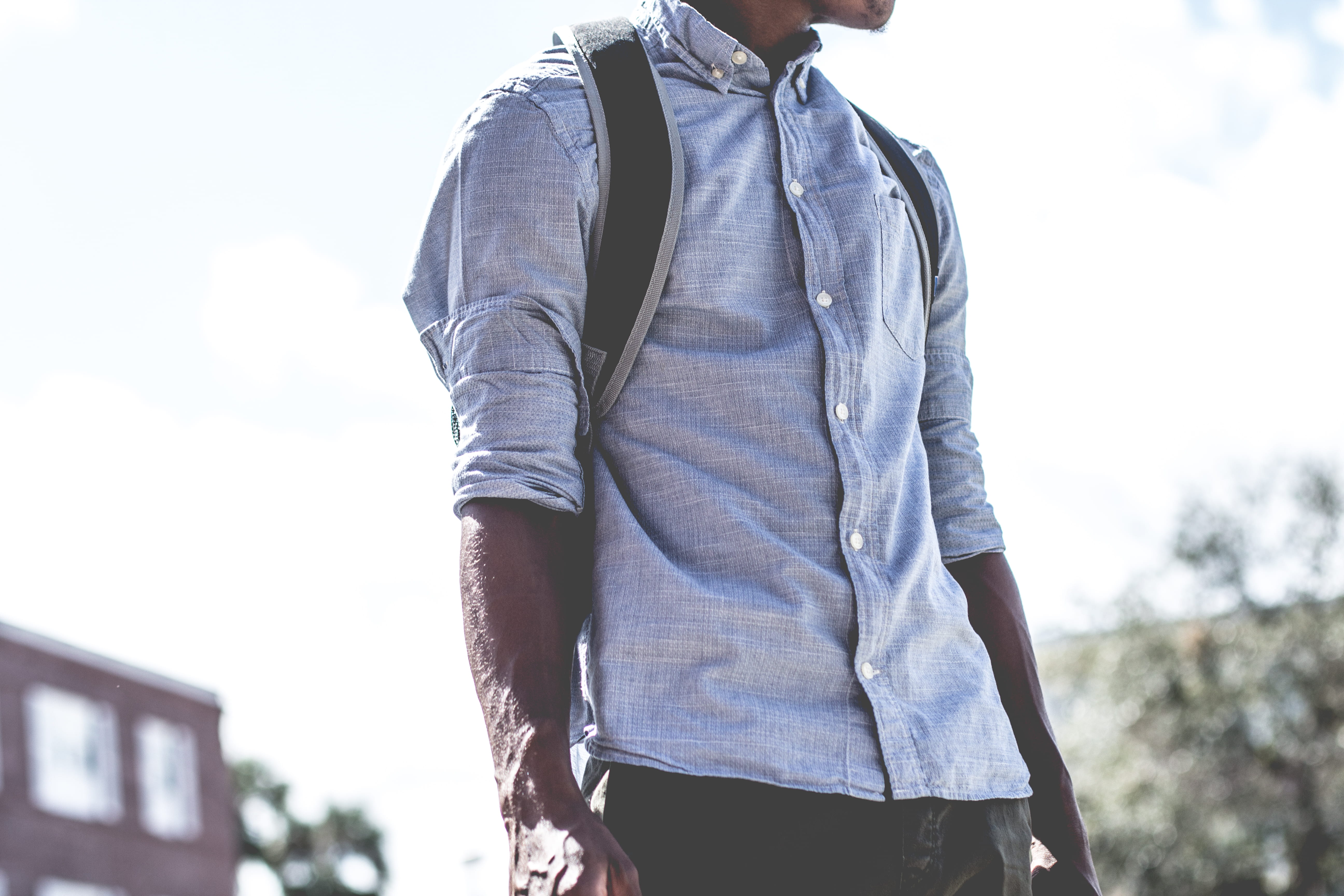 man standing carrying backpack, man wearing gray dress shirt and black backpack outdoors