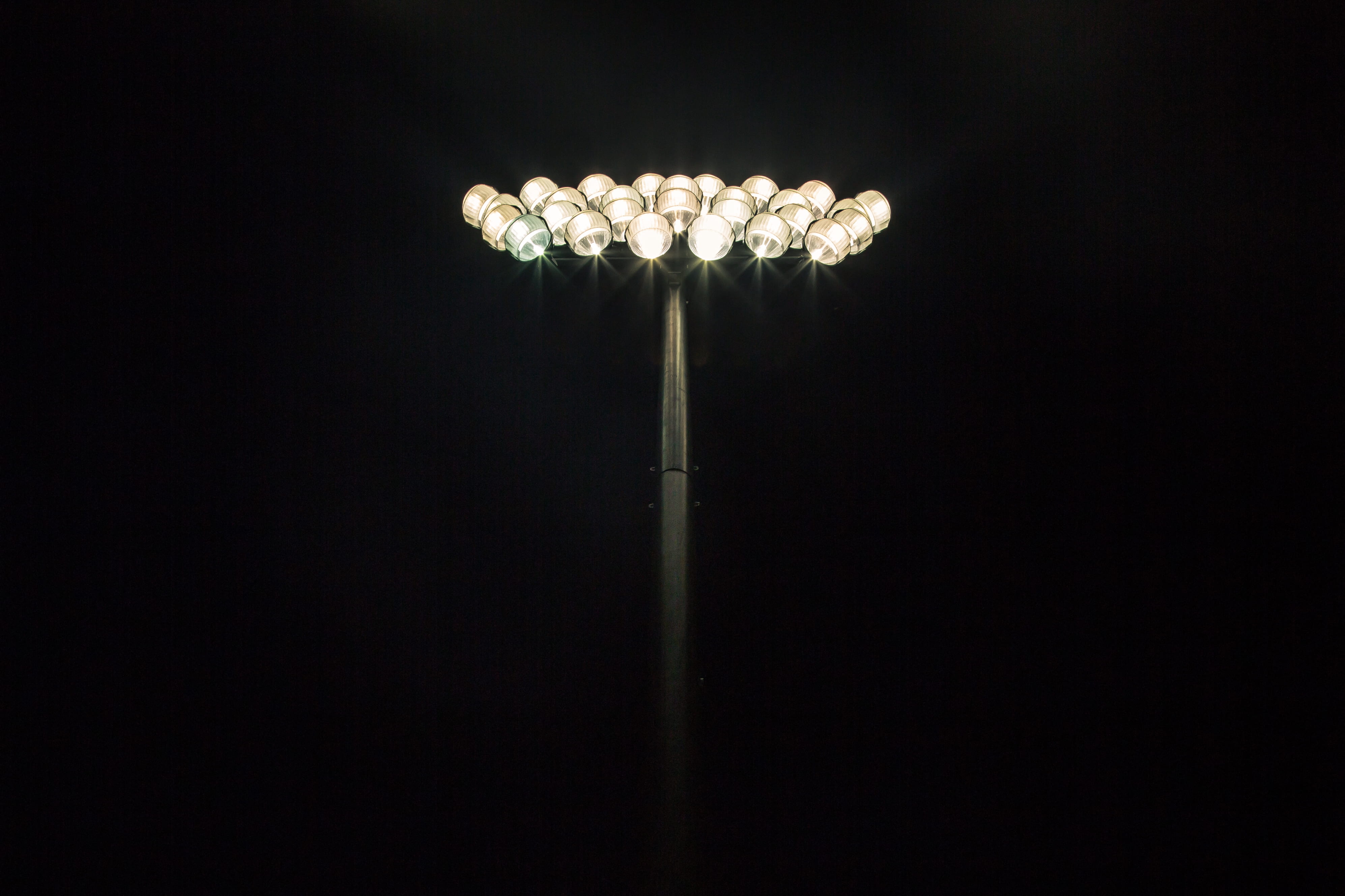 Floodlights shining at the top of a light pole with a pitch black background, untitled