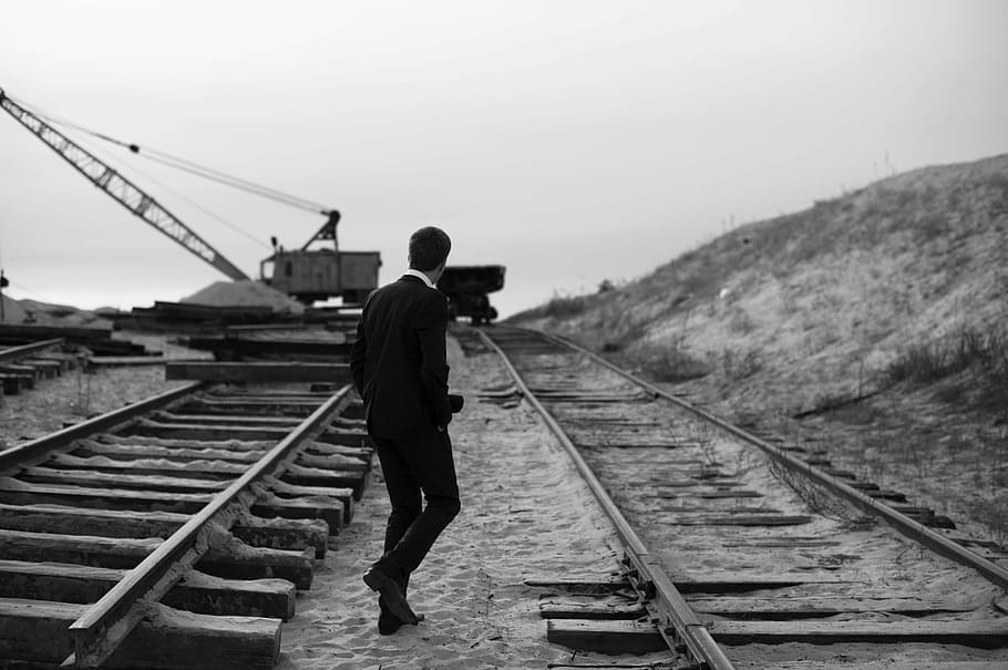 grayscale of man walking on train rail, grayscale photography of man walking between railroads HD wallpaper