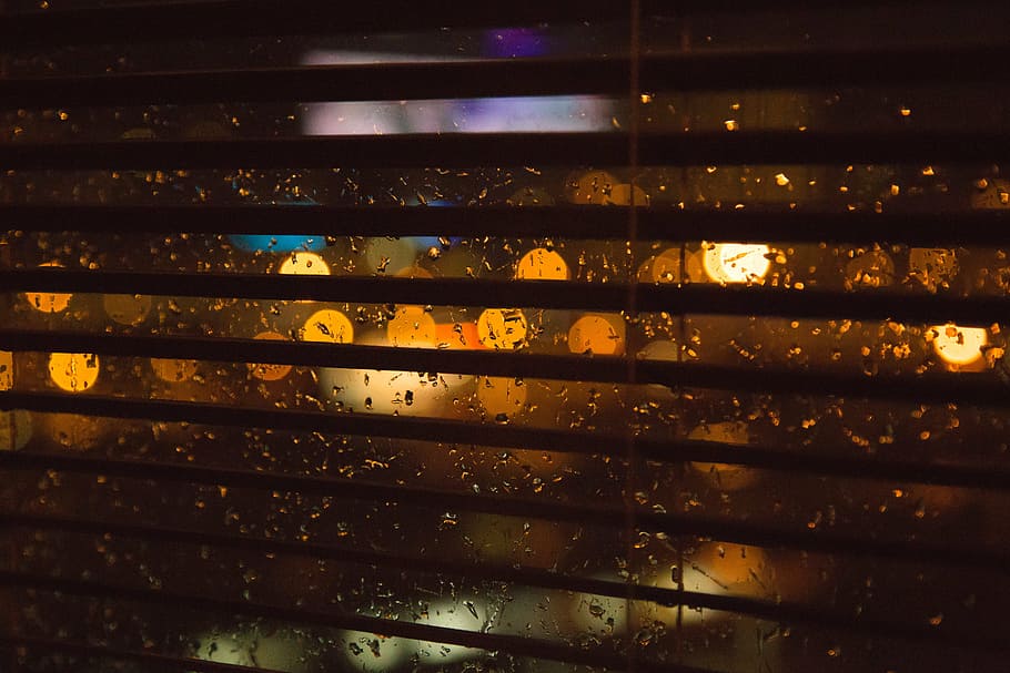 closeup photo of opened window blinds, blurry, lights, rain, dark