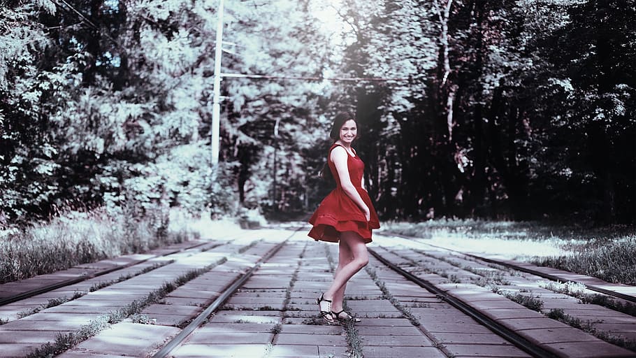 woman in red dress standing on pavement between trees photo, girl