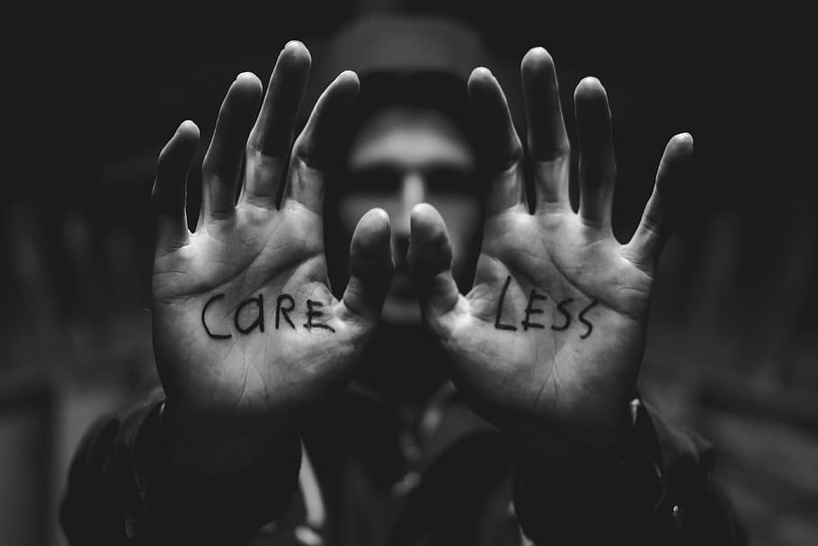 gray scale photography of man raising both hands with care less text on palm, grayscale photo of man wearing coat