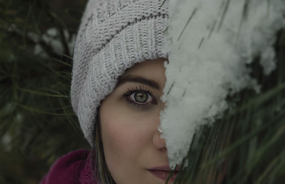 woman's face covered by green plant, woman wearing knit cap peeking on pine tree with snow HD wallpaper
