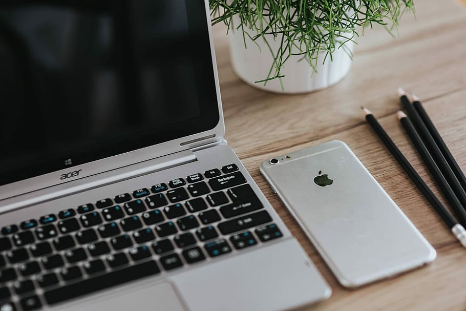 Silver Acer laptop on a wooden desk with a green plant, pencils and an Apple iPhone HD wallpaper