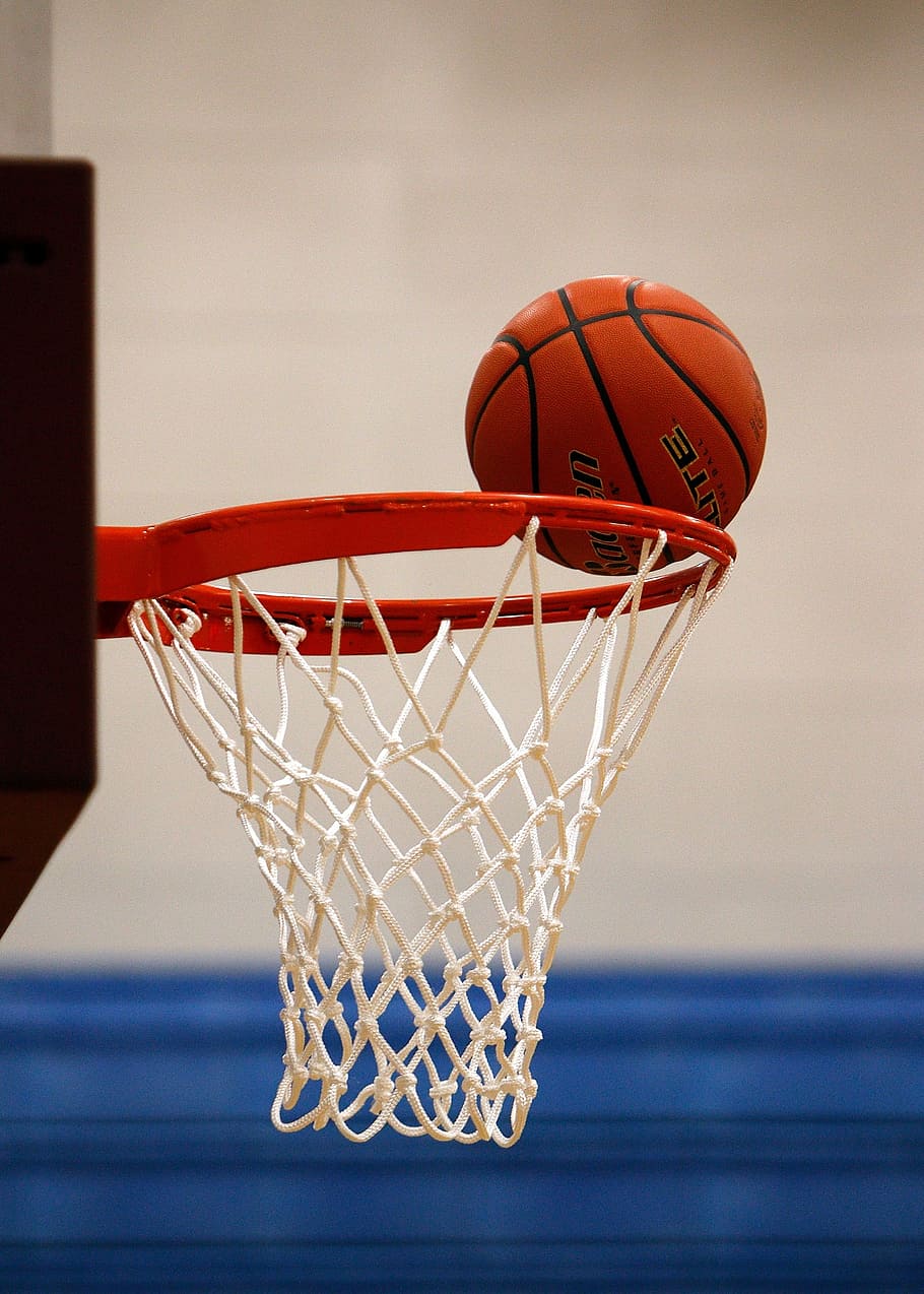 brown basketball on edge of white and red basketball hoop, net