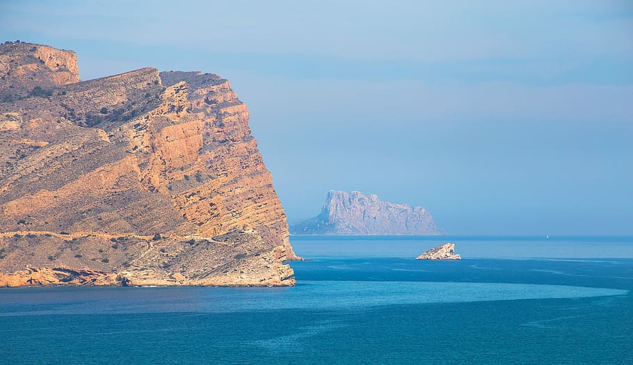 aerial photography of sea near mountain at daytime, photo of rock formations near body of water HD wallpaper