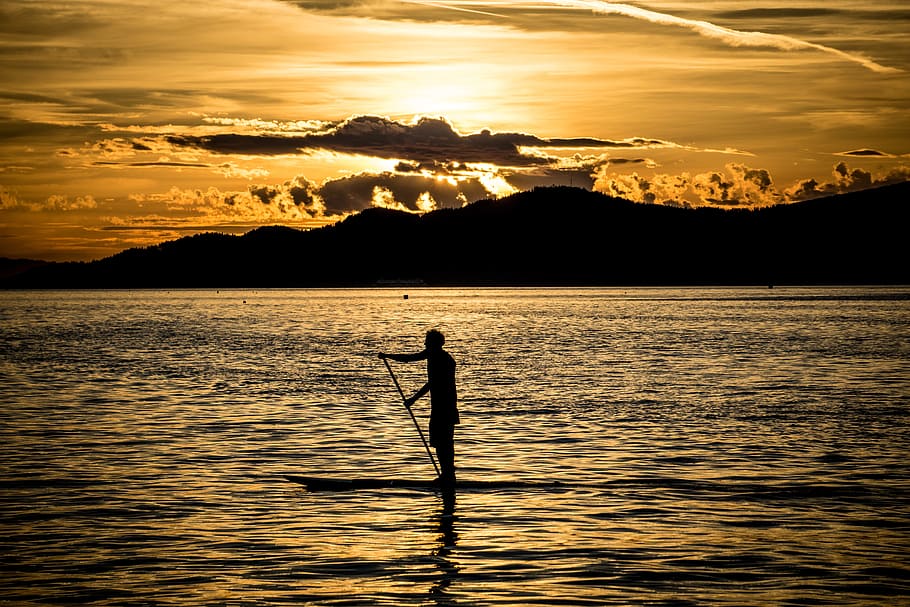 silhouette of person on boat surrounded by body of water, paddle board