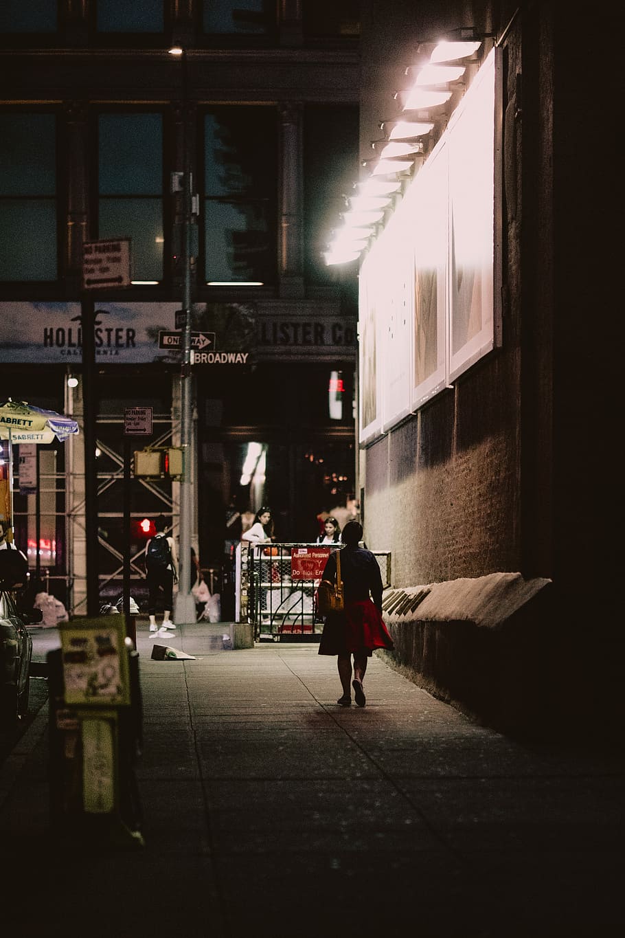 woman in black and red dress walking beside brown building, woman walking near brown wall