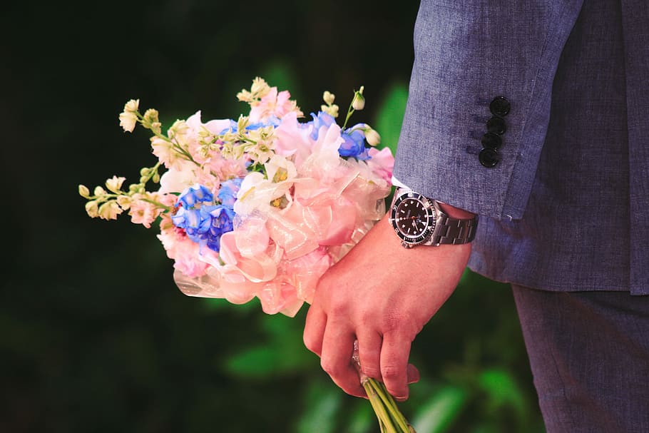 close up photography of man holding flowers, man holding pink and blue flower bouquet