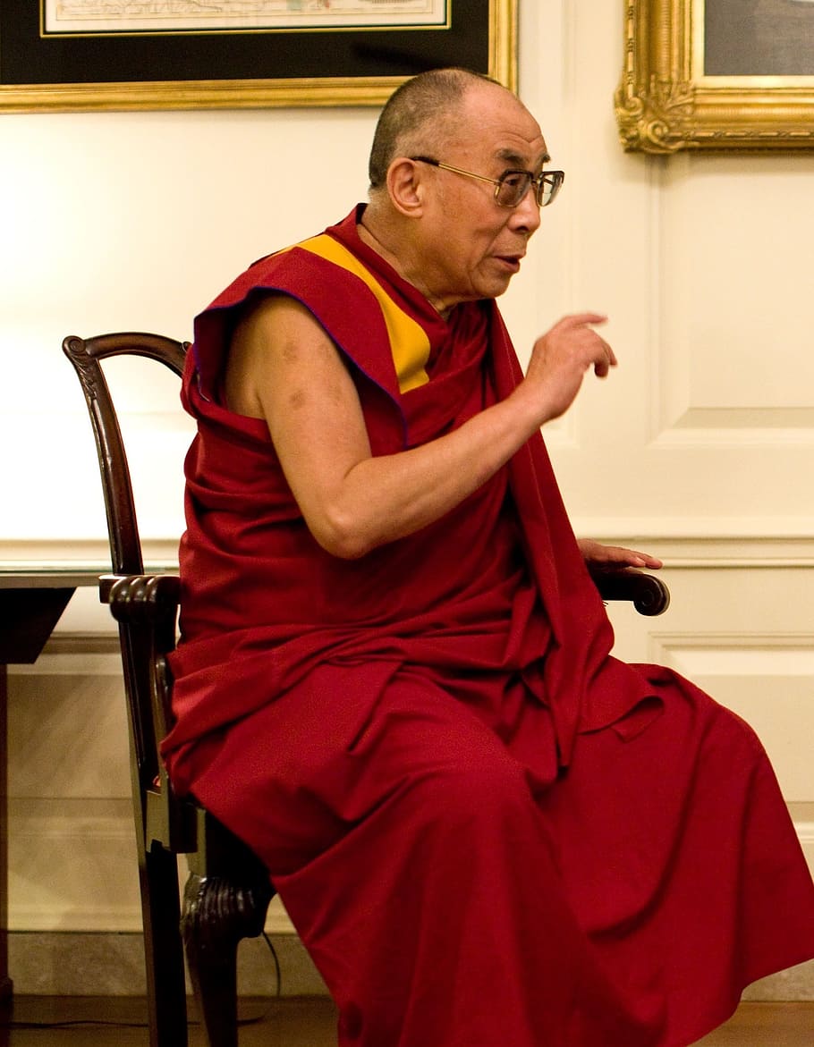 man sitting on armchair beside white concrete wall, dalai lama